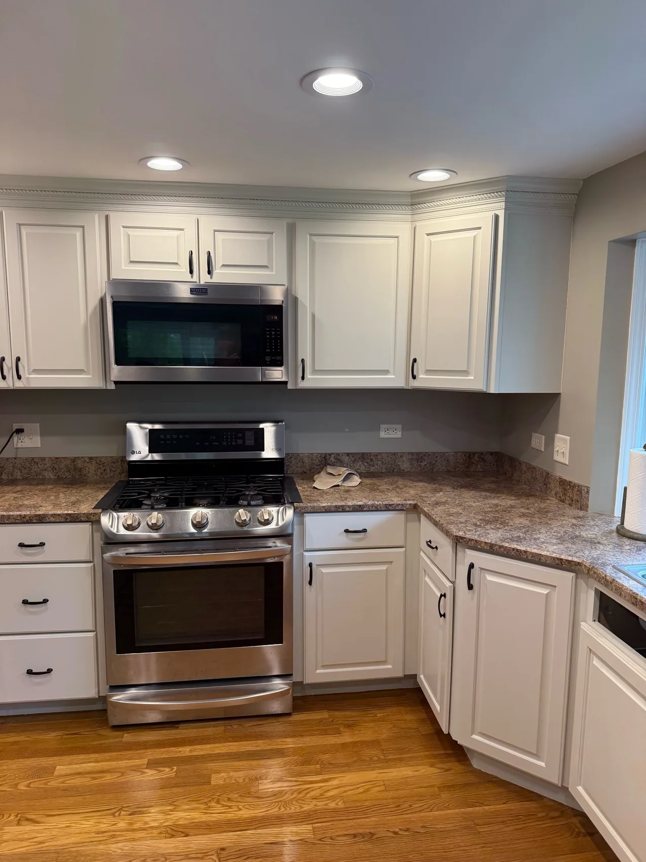 Finished cream-white raised panel kitchen cabinets with dark handles, granite counters, stainless appliances, and hardwood flooring