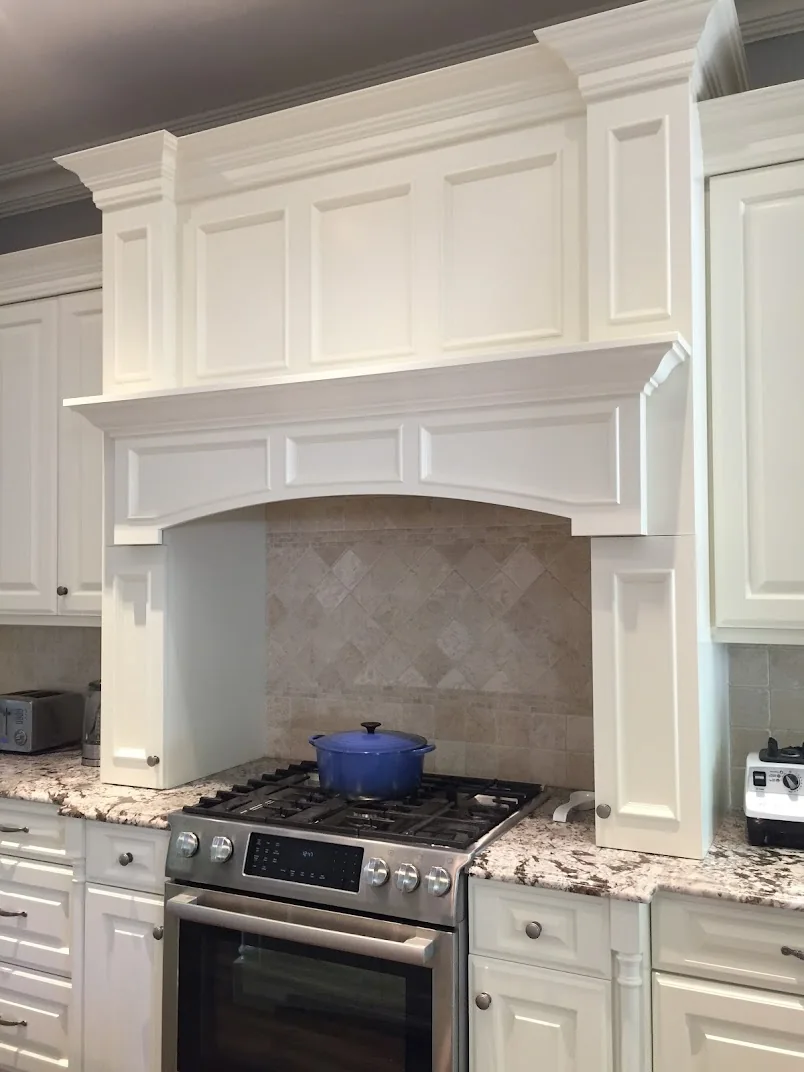 Finished white kitchen cabinets with raised panel doors, crown molding, and a decorative range hood around a gas cooktop