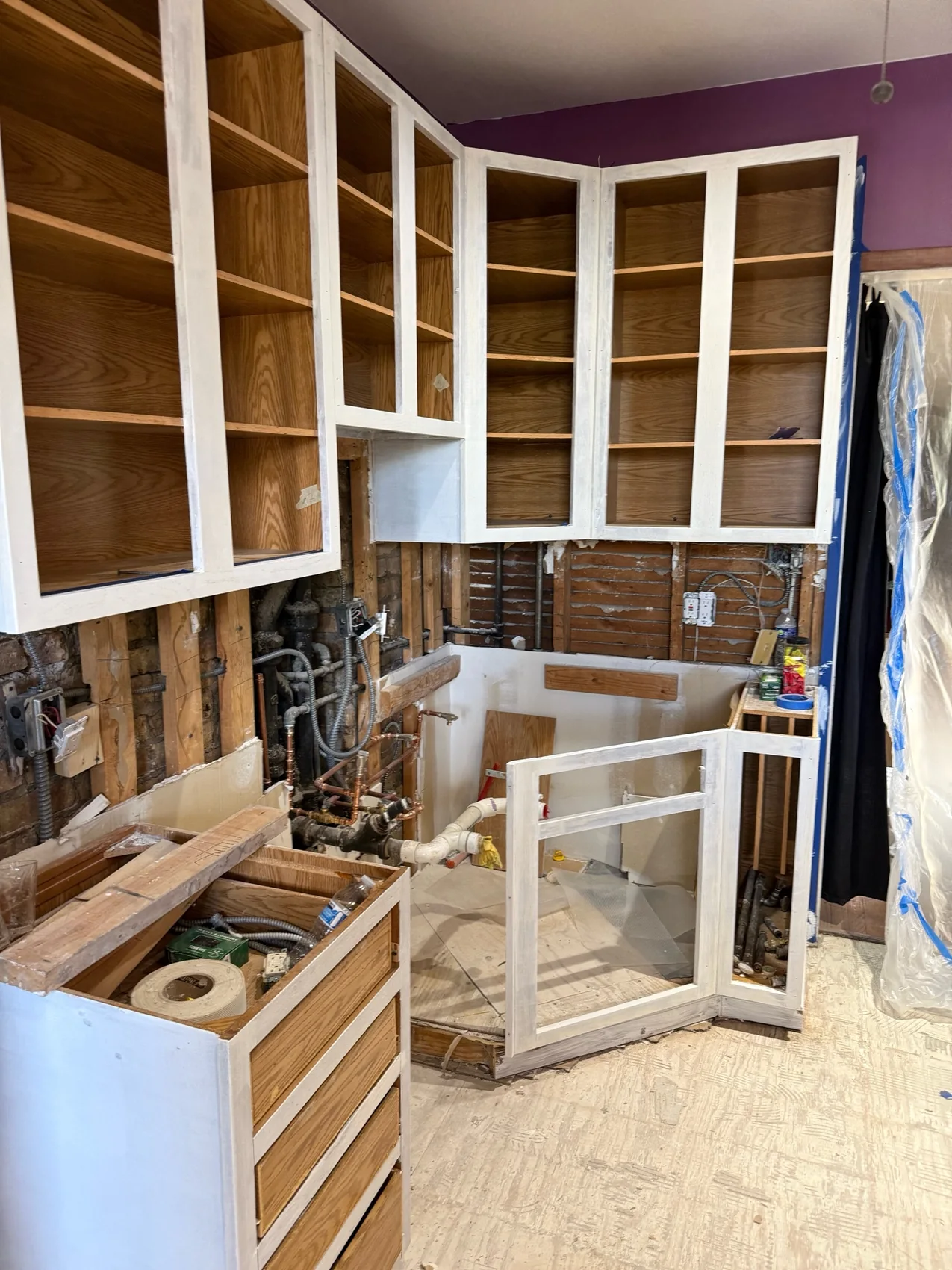 Cabinetry during preparation with doors removed, white primed face frames, wood grain interiors, and protected work areas