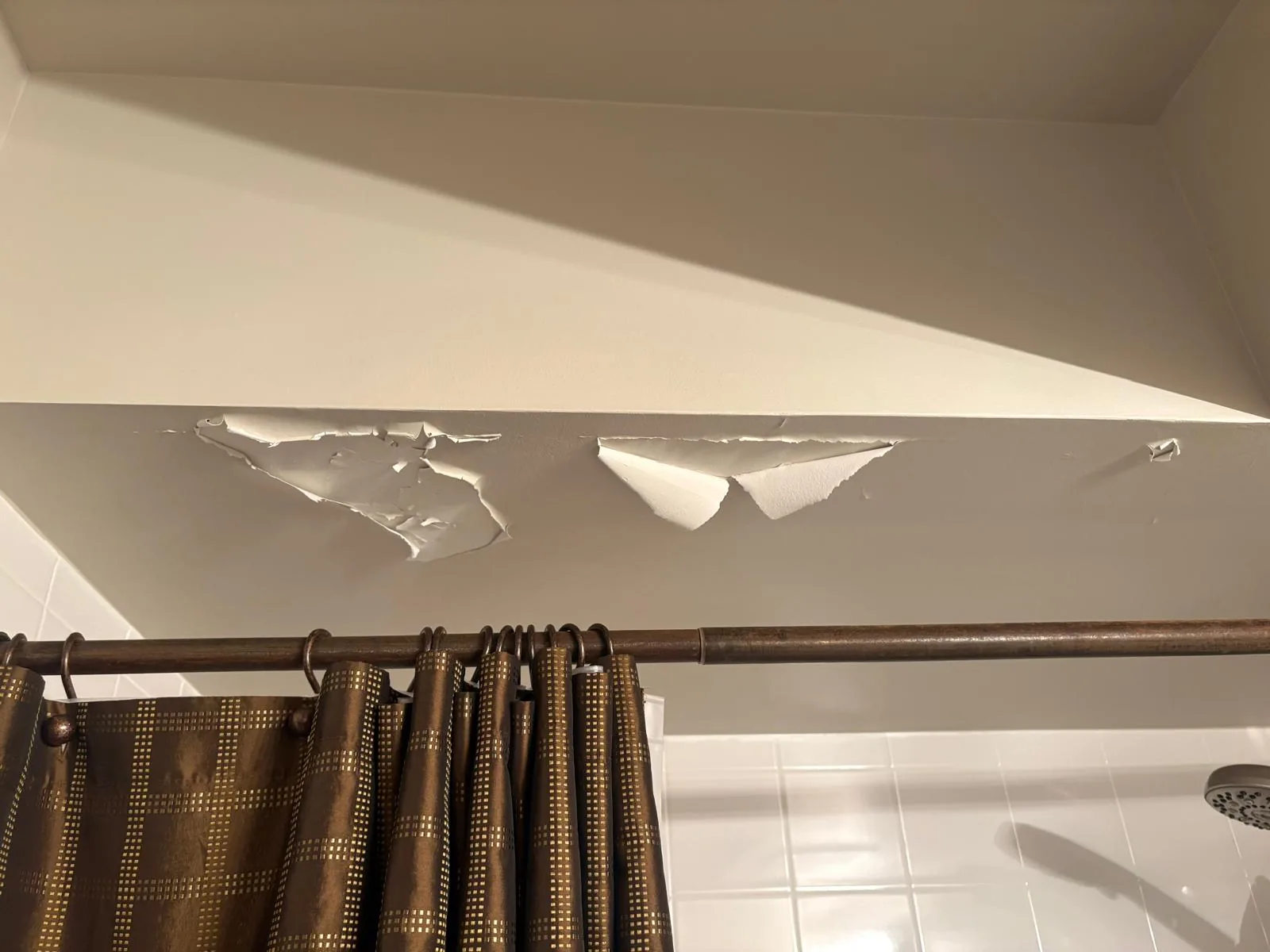 Before drywall repair, with peeling and damaged material above a tiled shower wall