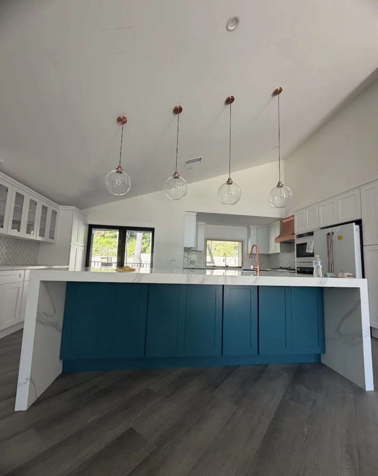 Finished kitchen with white perimeter cabinets and a deep teal-blue painted island beneath glass globe pendants
