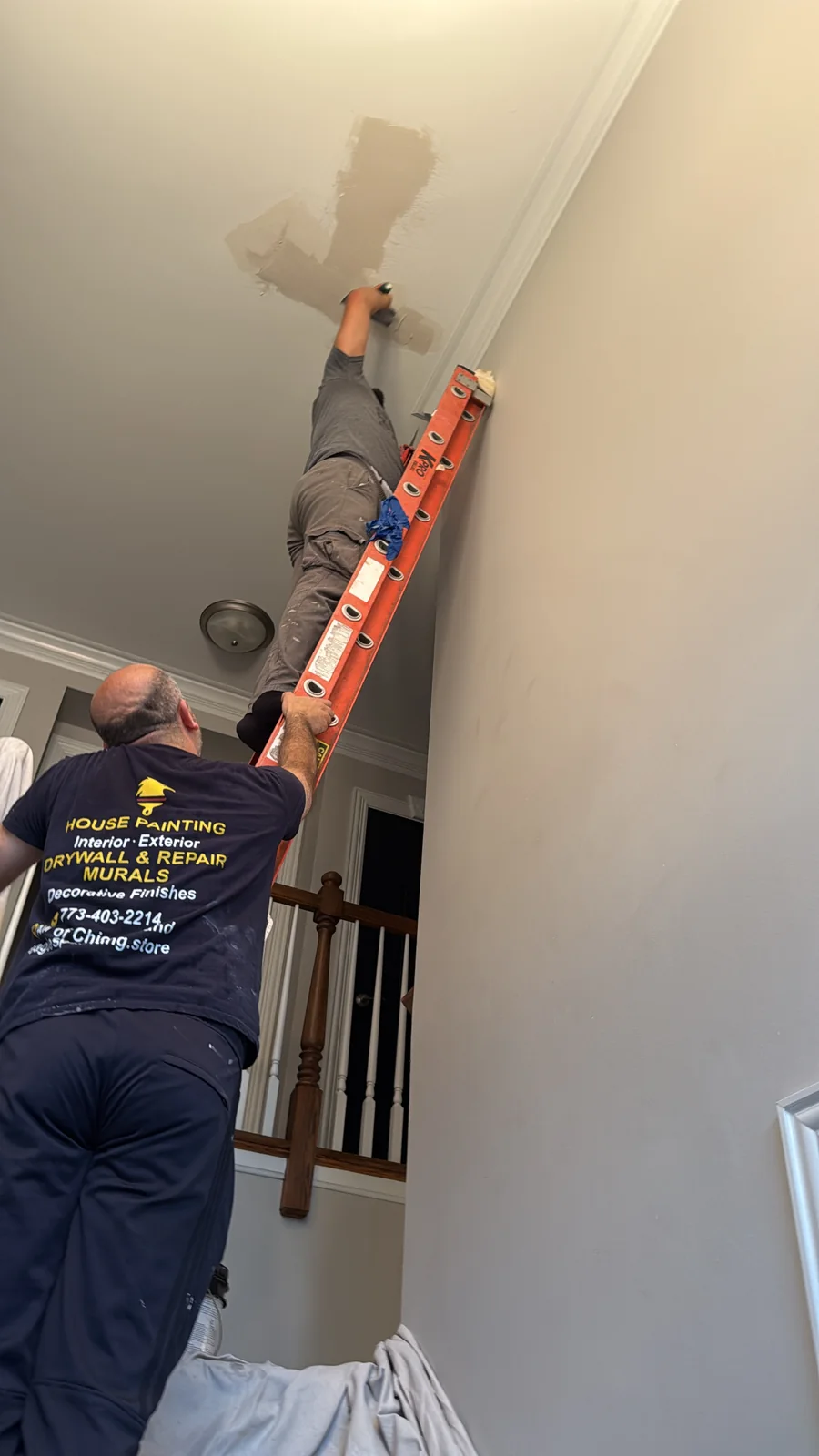 Eagles drywall repair team patching a high ceiling above an interior staircase