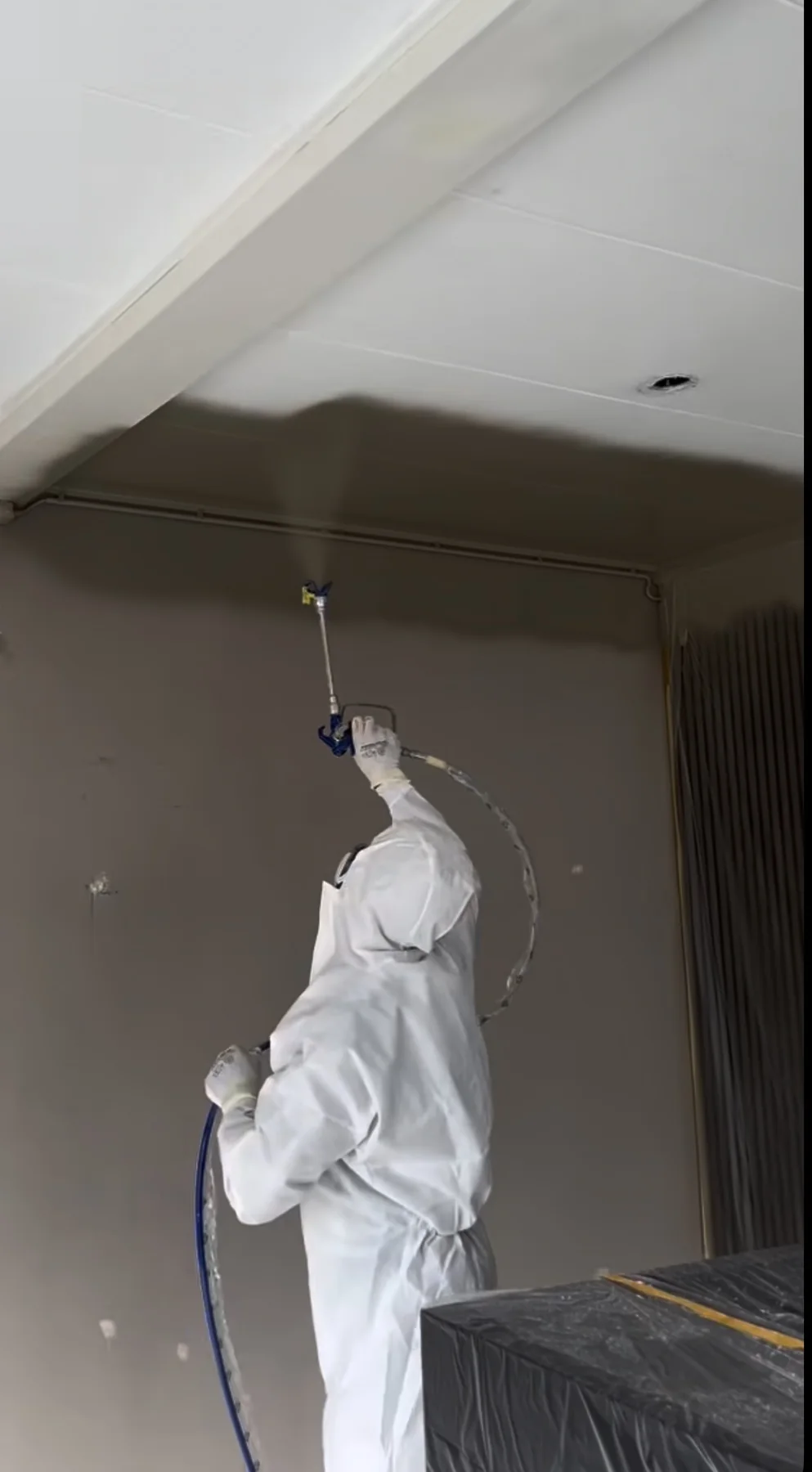 Painter in protective coveralls spraying a ceiling above protected furnishings