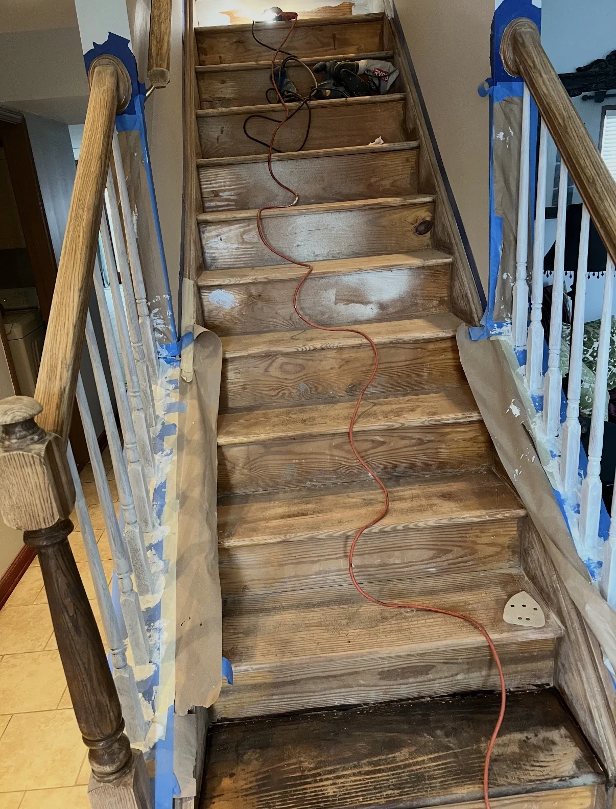 Before interior painting, showing a wood staircase with masked rail components and sanding equipment during preparation