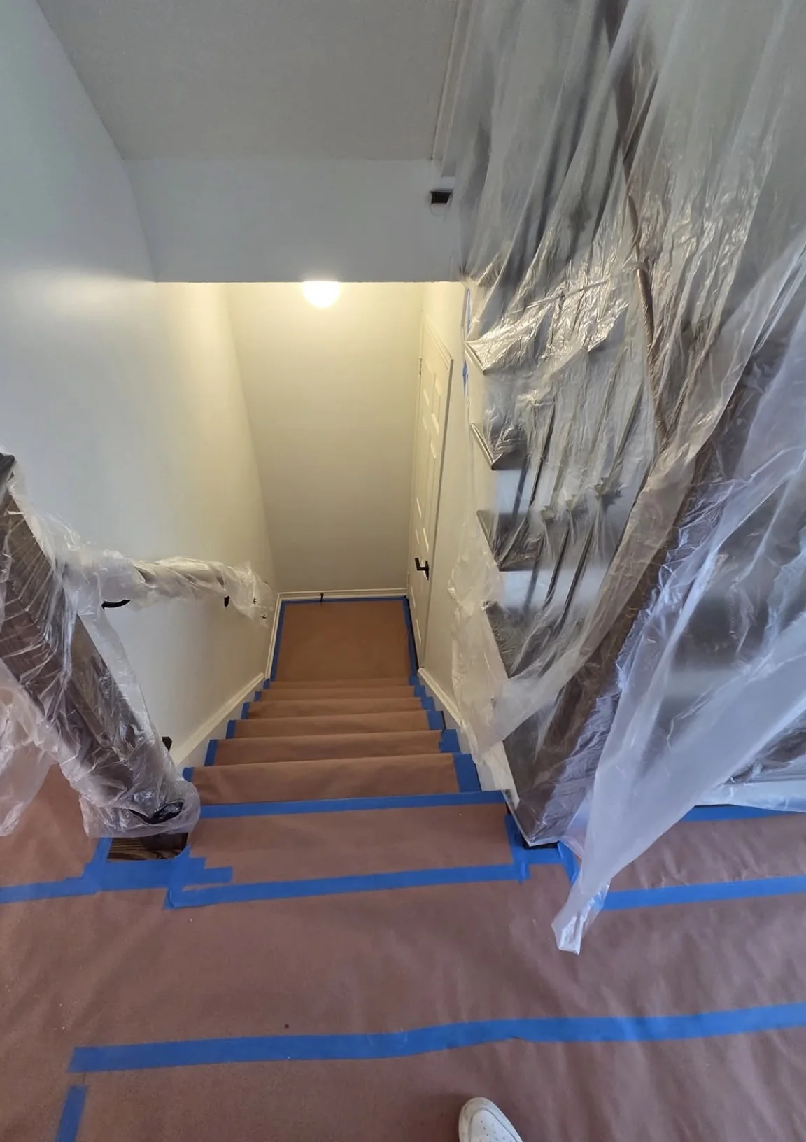 Residential stairwell fully protected with paper, plastic, and blue tape before interior painting