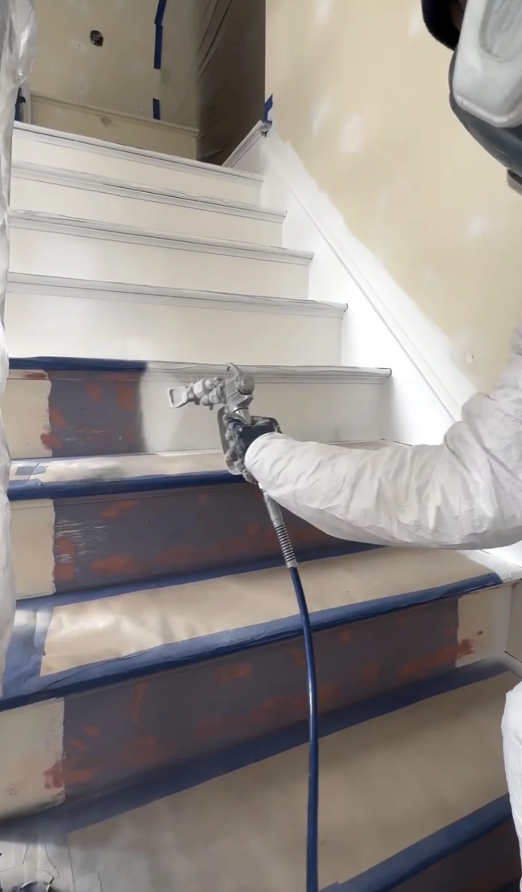 Painter applying a sprayed coating to masked stair risers during interior preparation