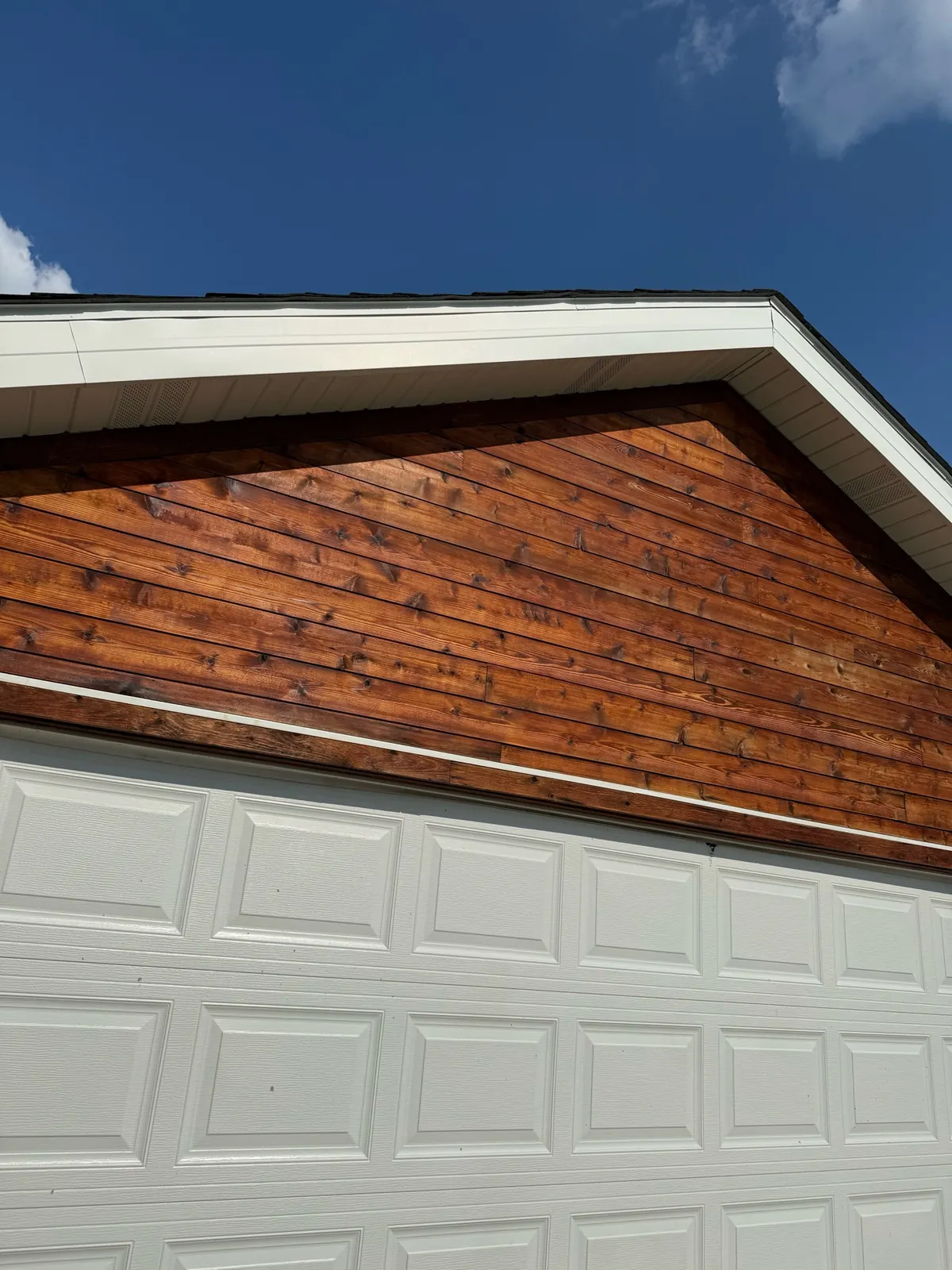 Wood sided exterior gable with white fascia and trim above a paneled garage door