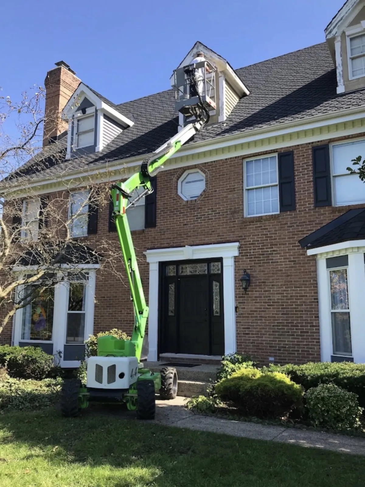 Exterior crew using a boom lift to reach upper trim on a multi story brick home
