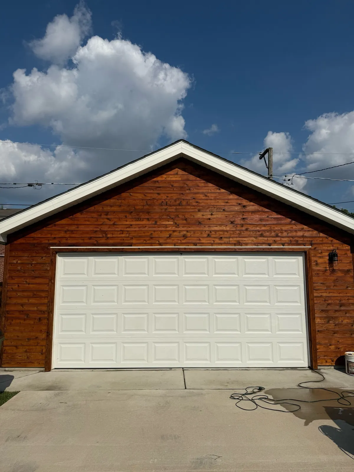 Wood sided garage exterior with white trim, hose, and equipment during final field cleanup