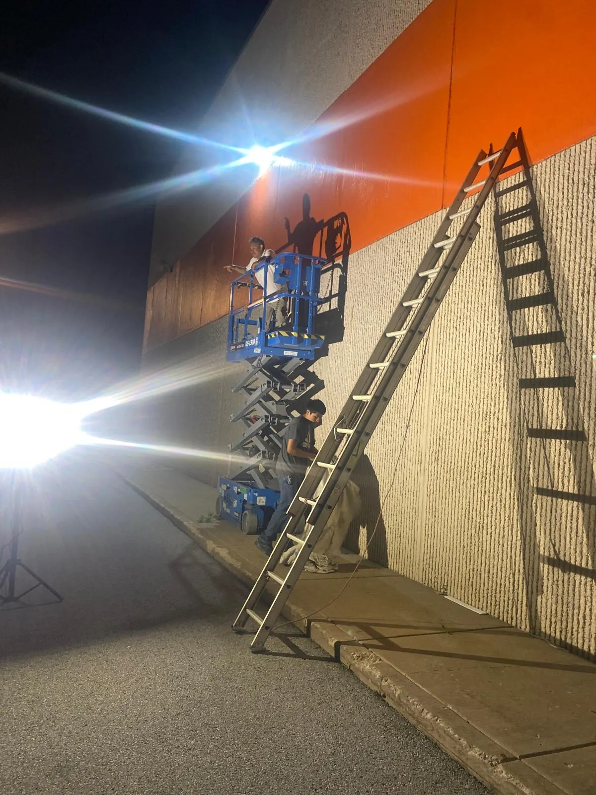 Exterior painting crew using a lift and ladder during a nighttime production shift