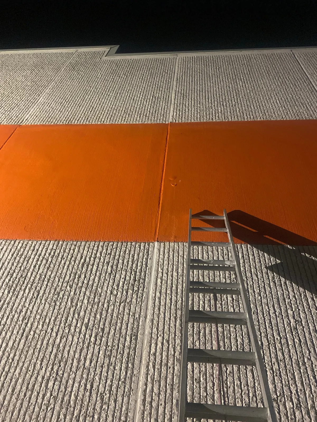 Close view of an orange coating applied across a ribbed exterior surface beside an aluminum ladder