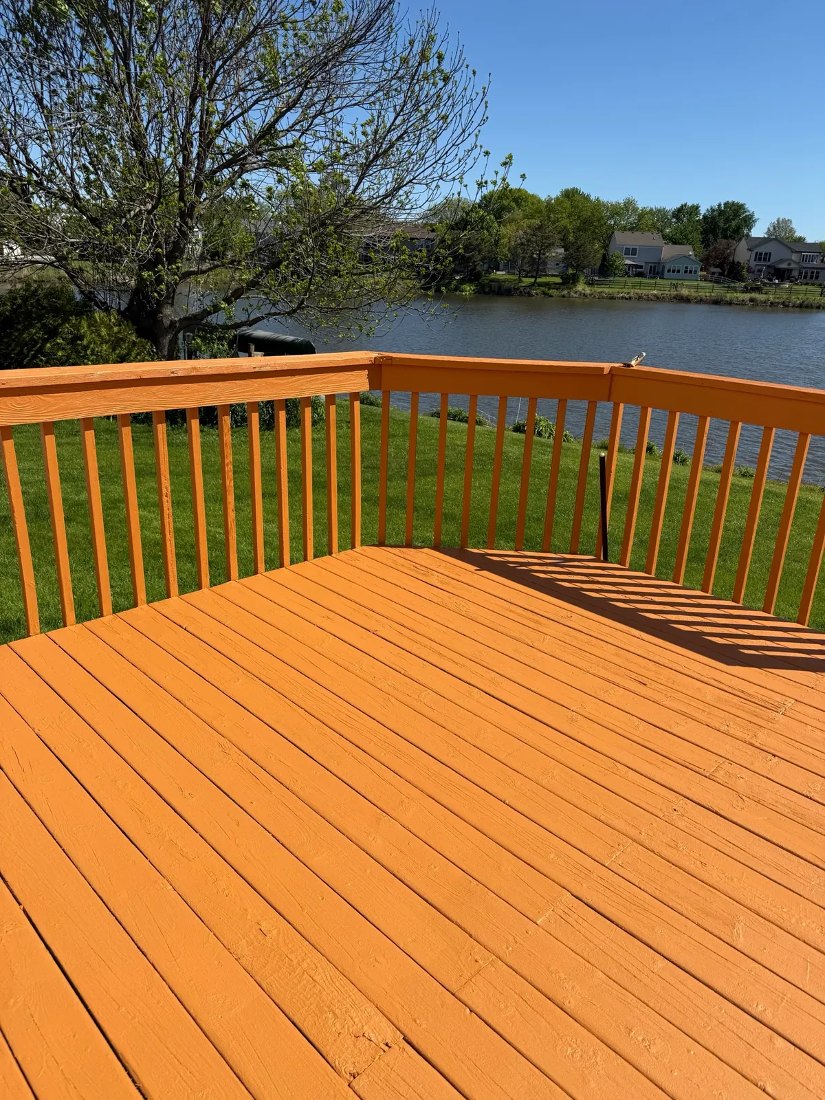 Finished warm-toned wood deck and railing overlooking a landscaped waterfront