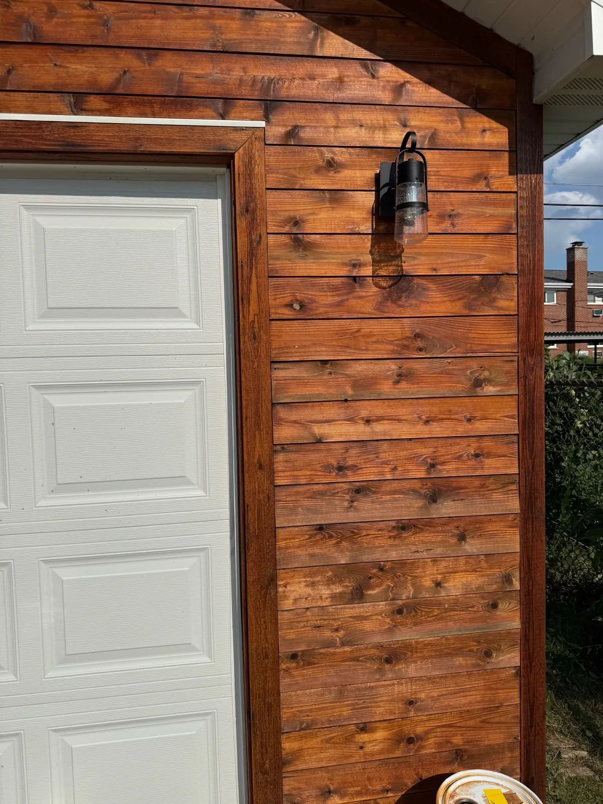 Close view of warm wood siding and trim beside a white paneled garage door and black exterior lantern