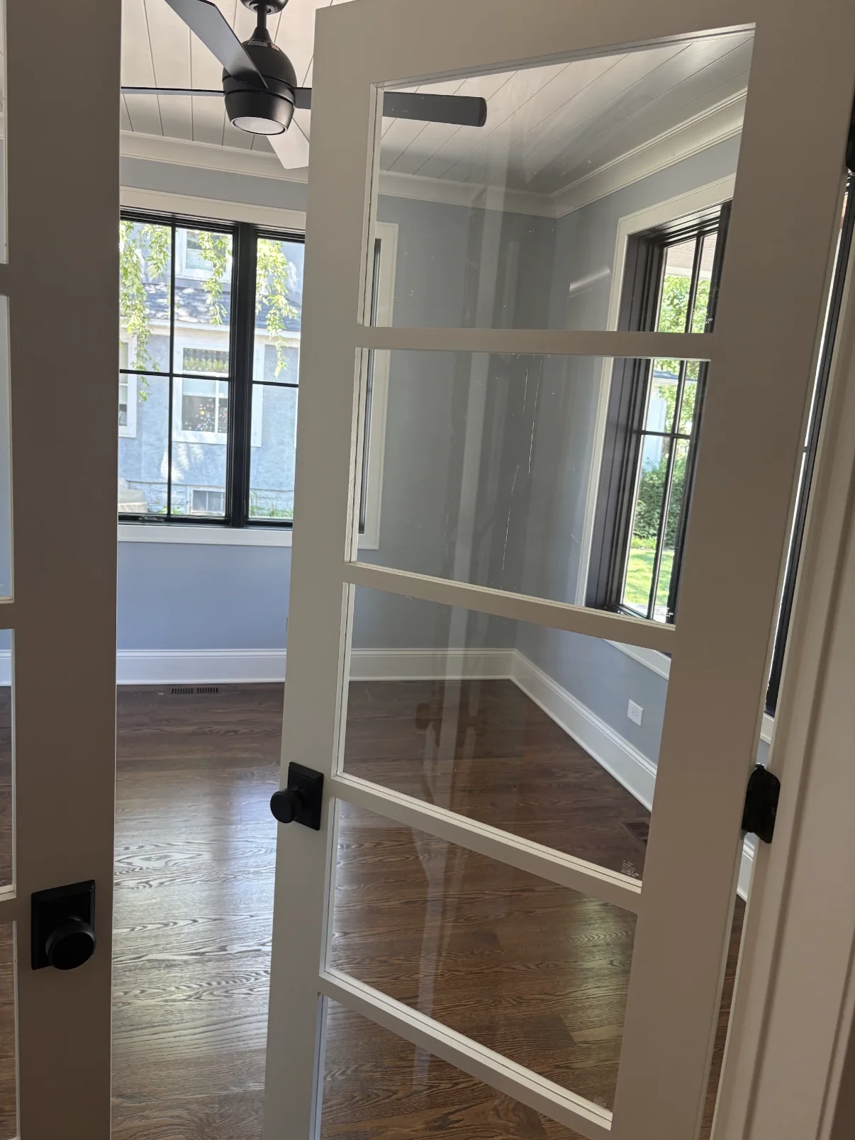Finished light blue gray room with white glass paneled doors, black window frames, white trim, and dark wood flooring