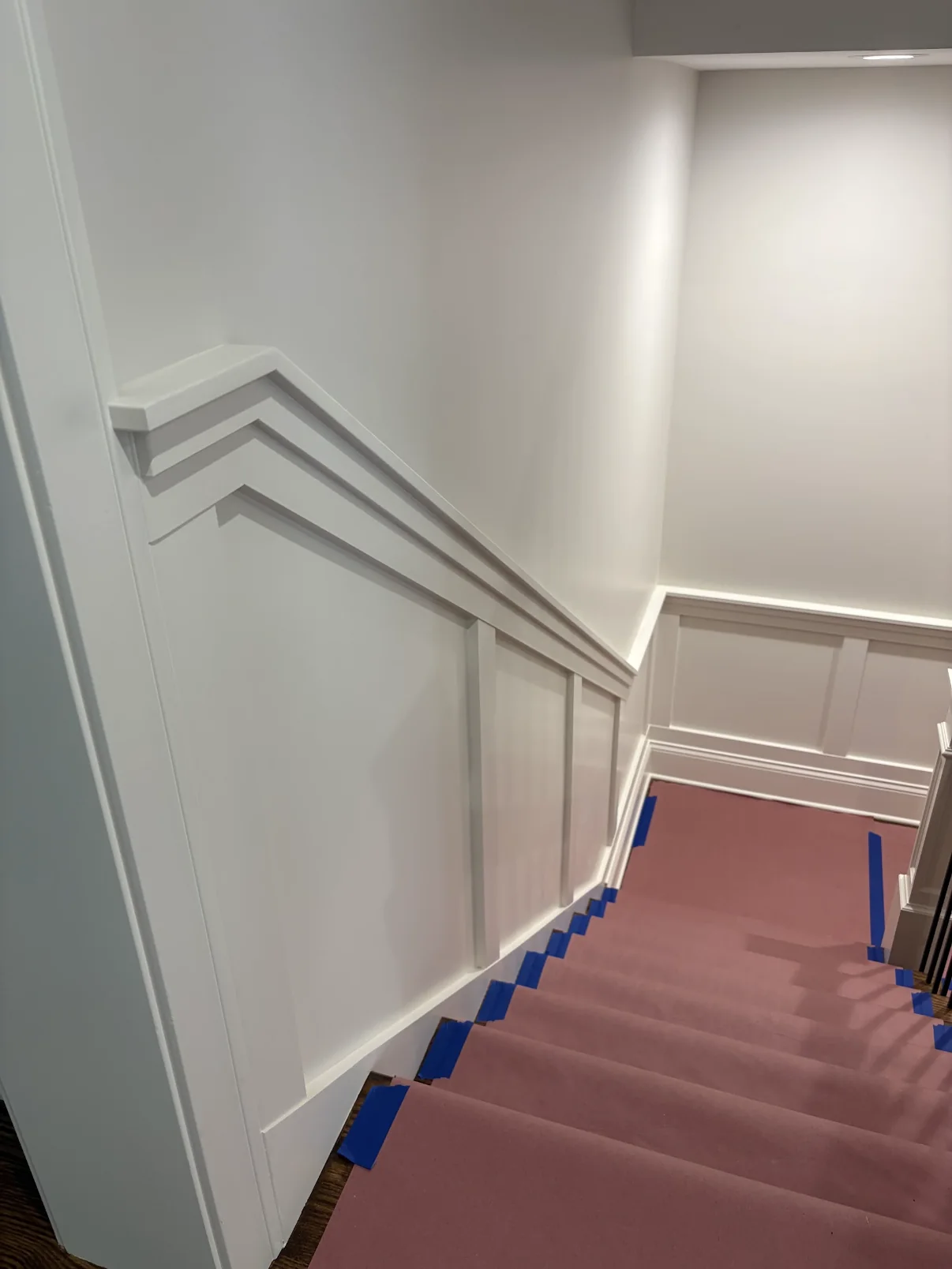 Fresh white staircase paneling and trim with treads and landings protected by paper and blue painter's tape