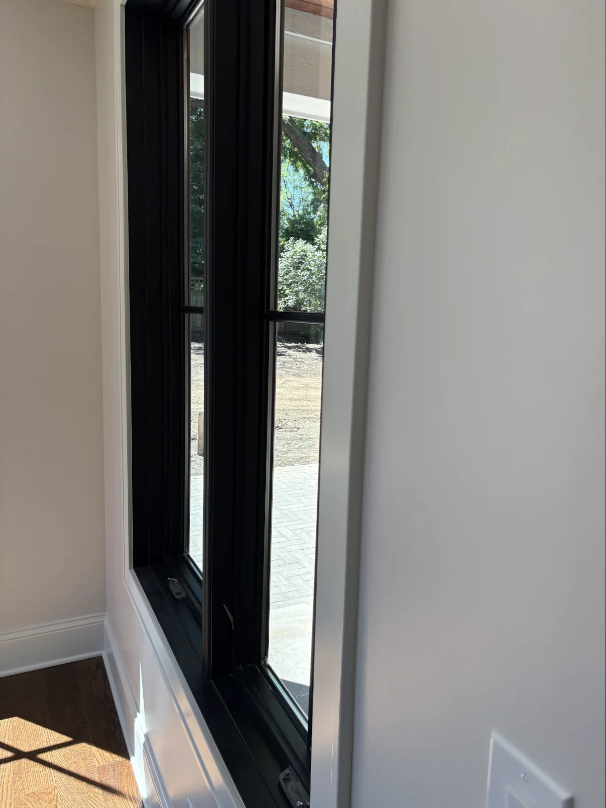Crisp white interior wall and trim beside a black framed window and dark wood floor