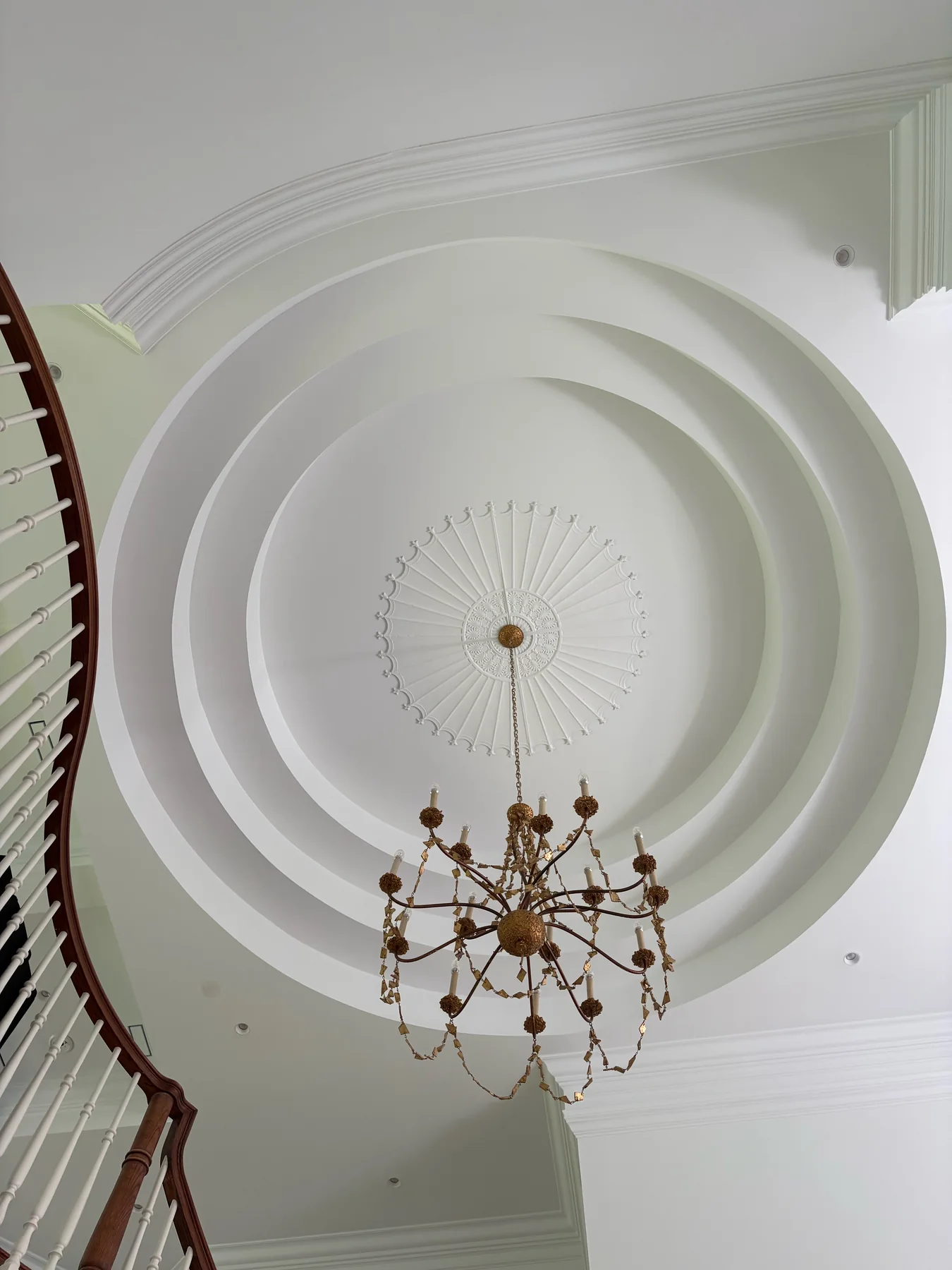 Ornate white tray ceiling with layered crown molding, decorative medallion, chandelier, and stair railing