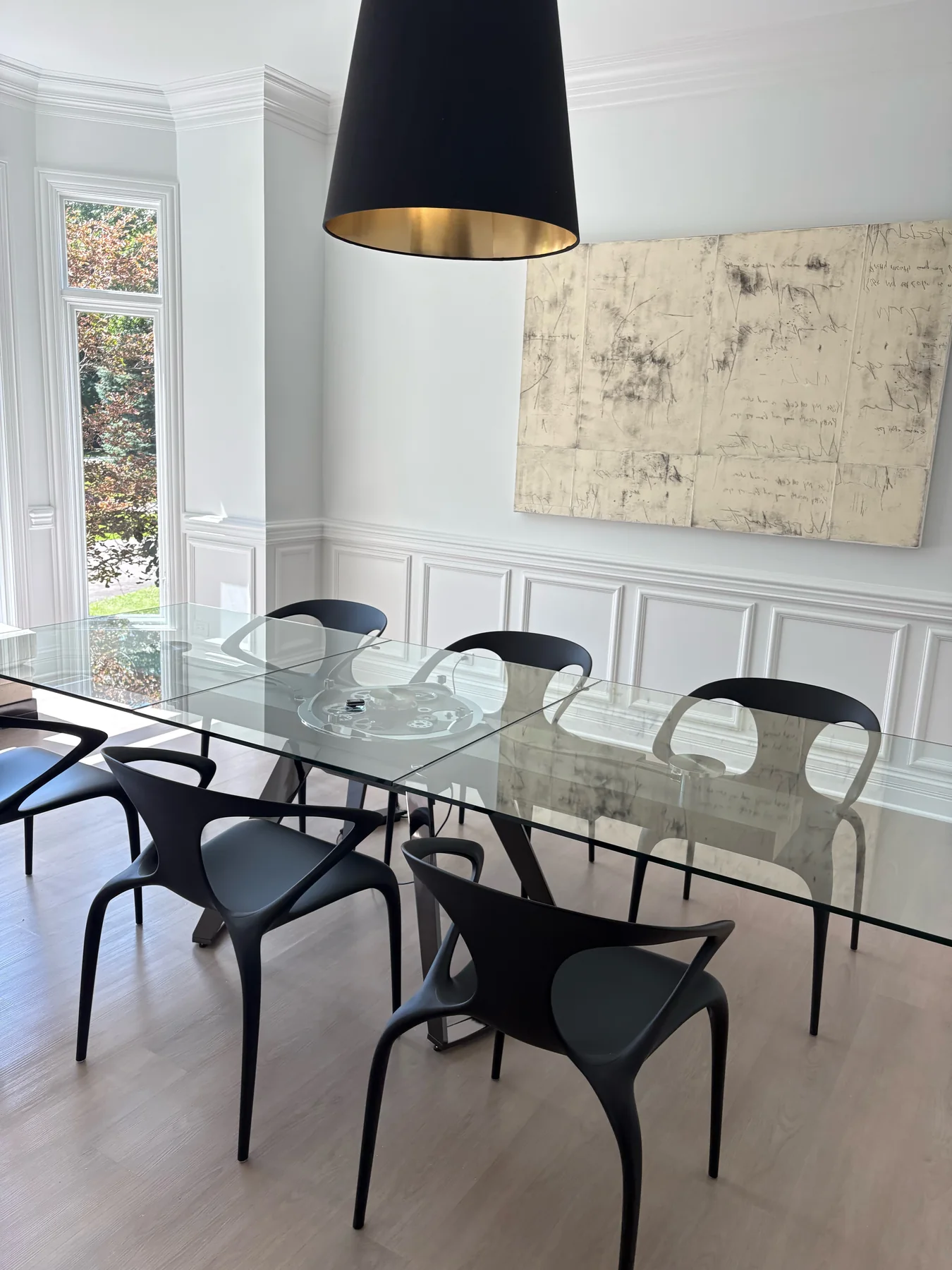 Finished dining room with pale neutral walls, white wainscoting and crown molding, and a glass dining table