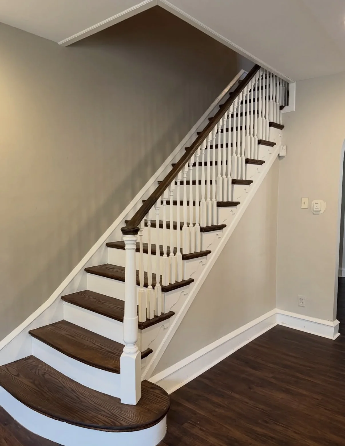 Painted residential staircase with neutral walls, white trim and balusters, and dark wood treads