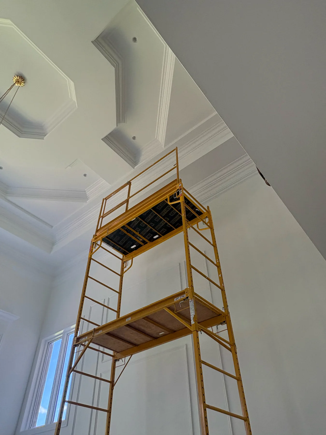 Rolling scaffold positioned beneath ornate ceiling trim in a high ceiling interior