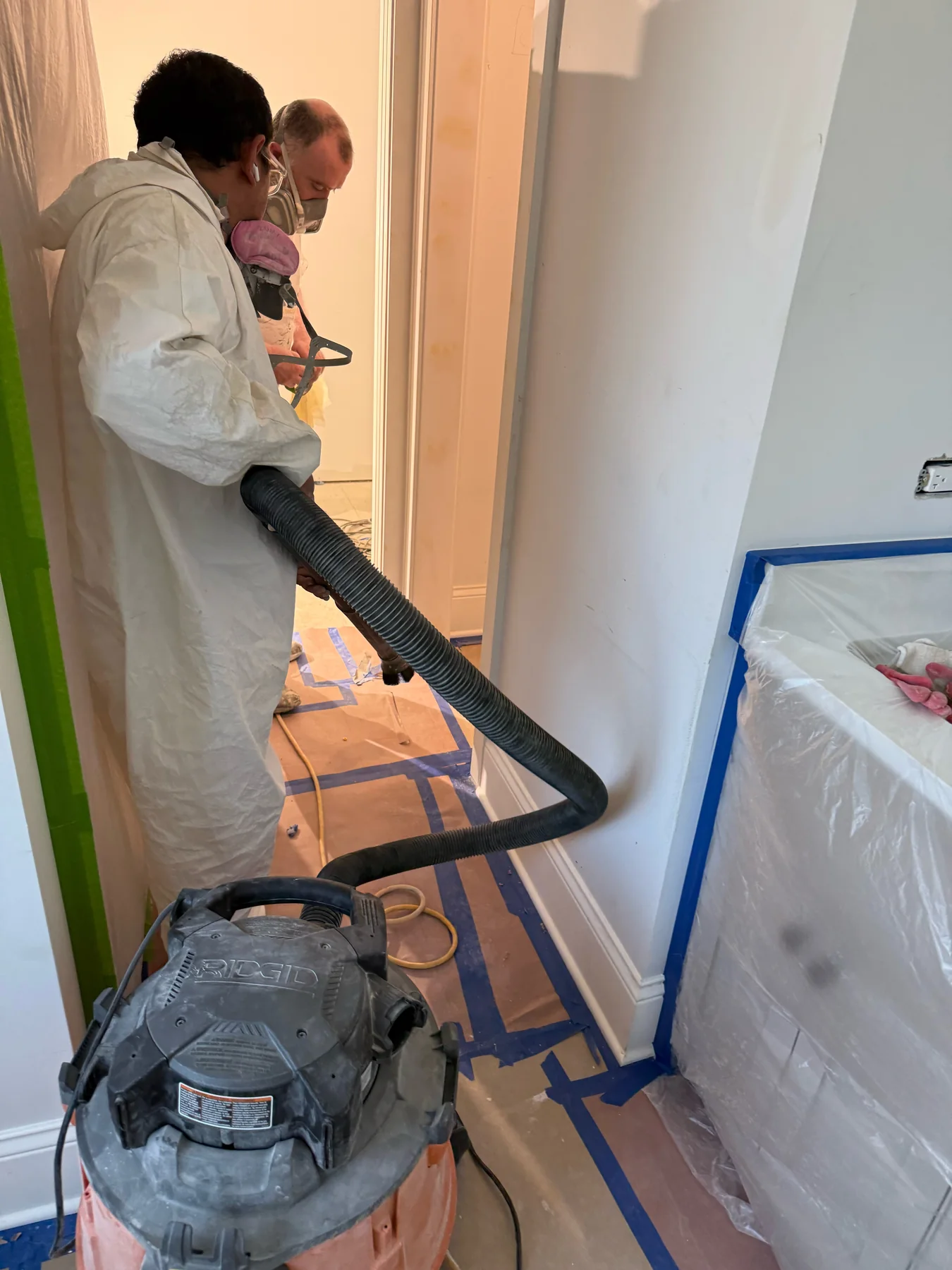 Painting team in protective equipment preparing a masked interior hallway with dust-control equipment
