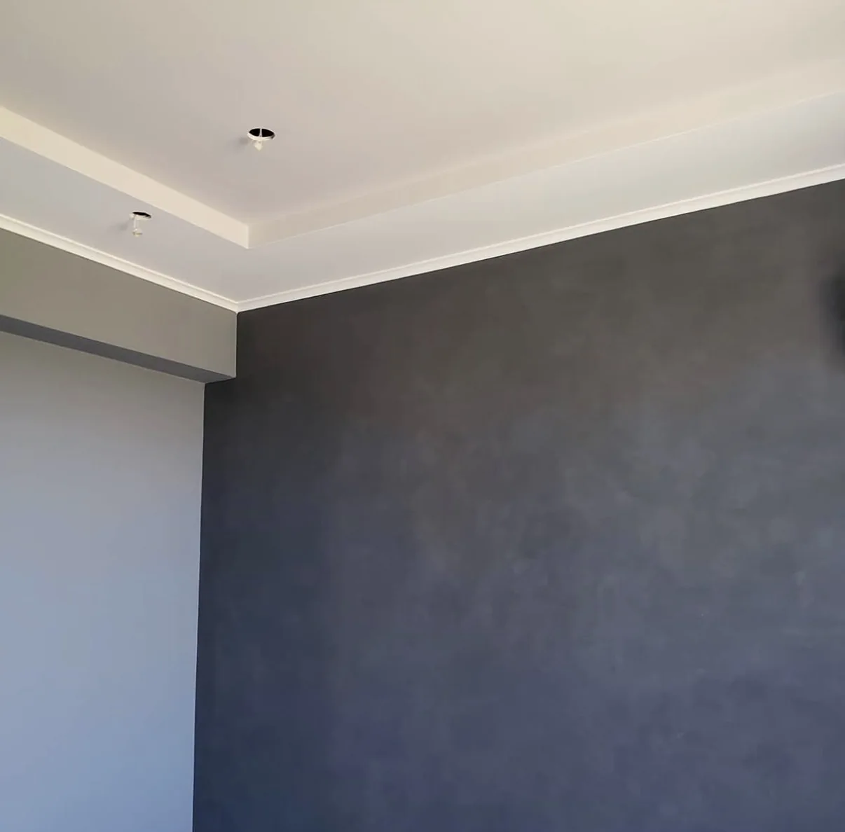 Dark charcoal limewash feature wall beneath white crown molding during an interior installation