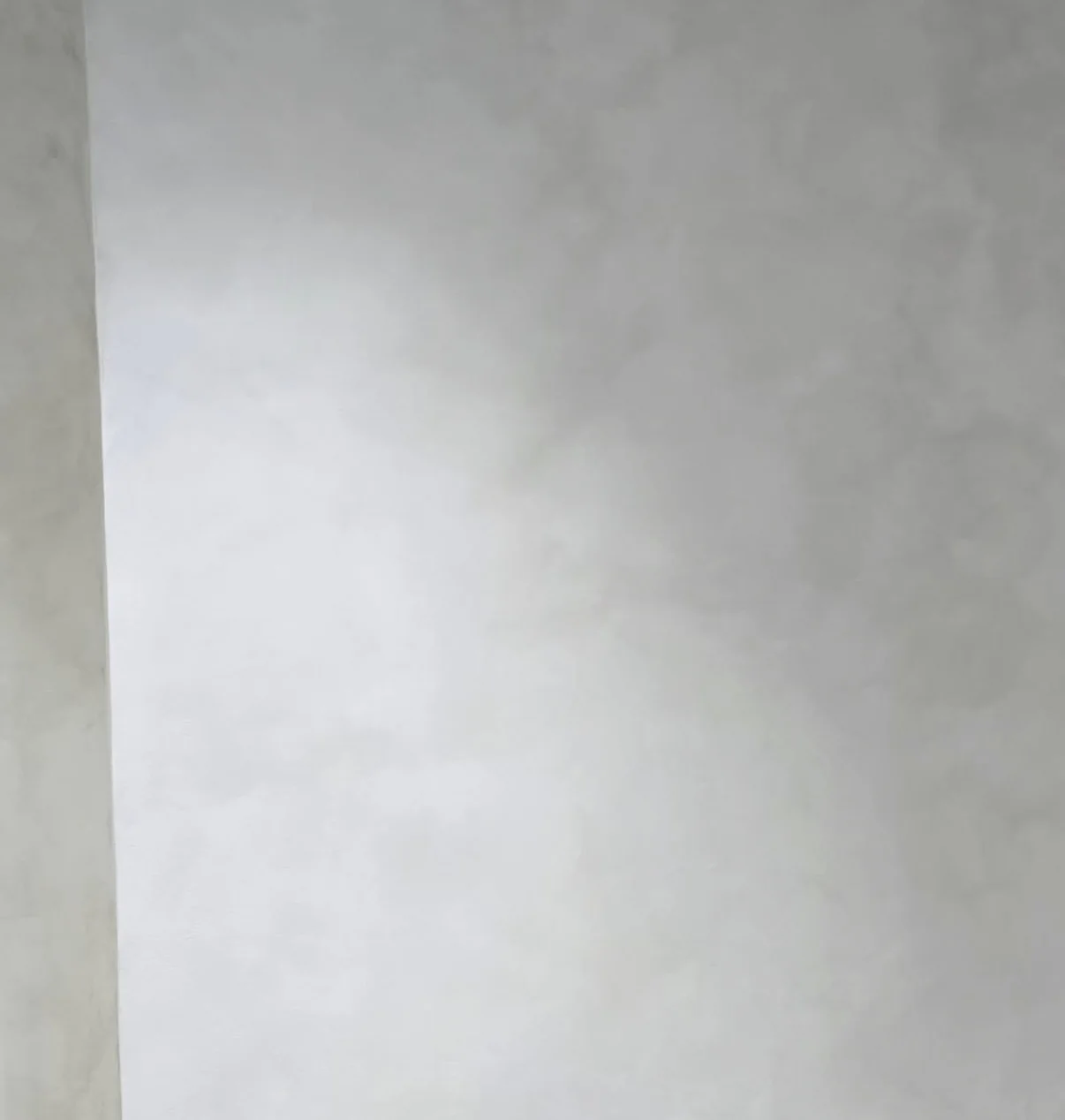 Close-up of a pale gray white limewash wall with subtle mottling beside a vertical corner edge