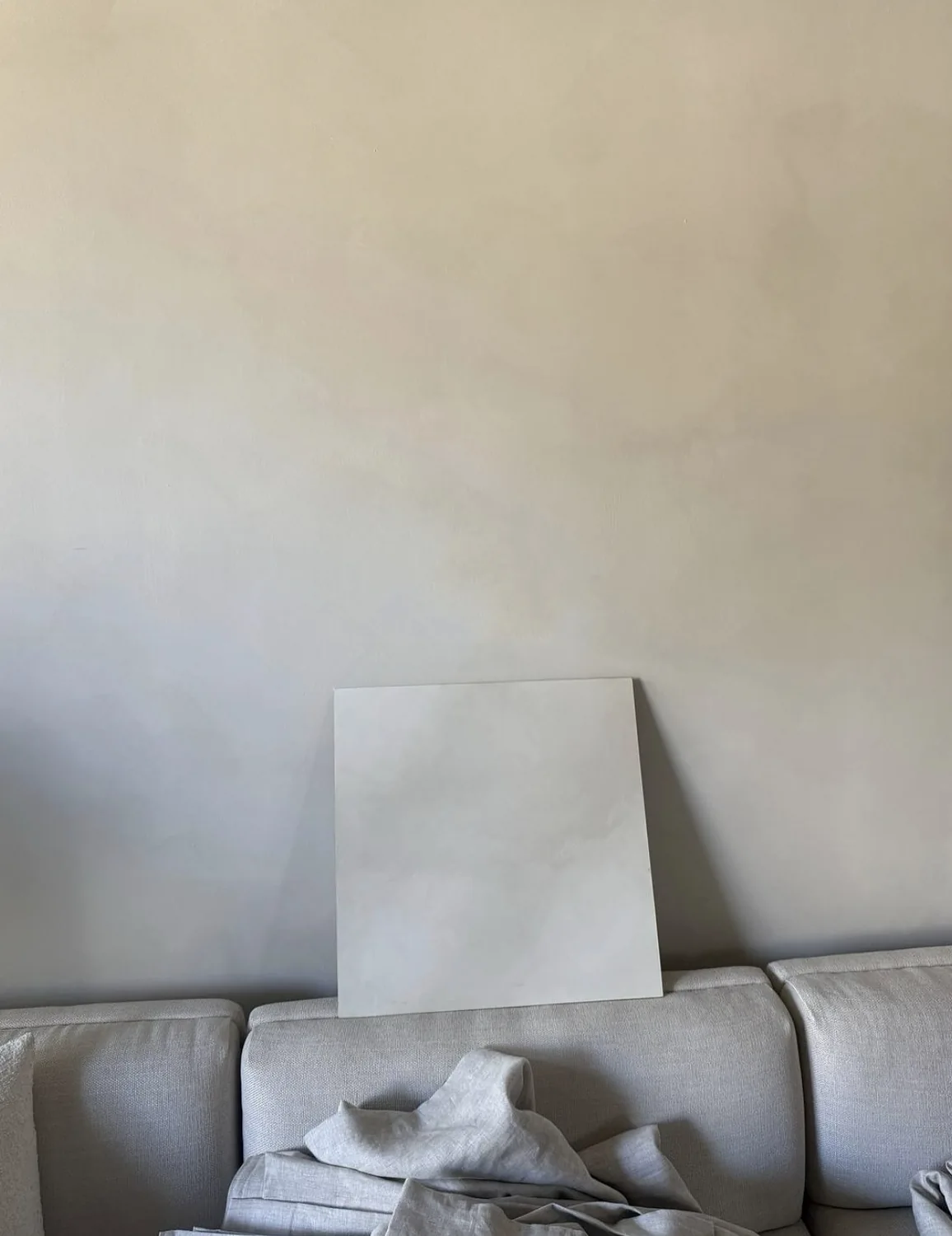 Subtle beige limewash wall above a light sofa with a pale sample board leaning against the finished surface