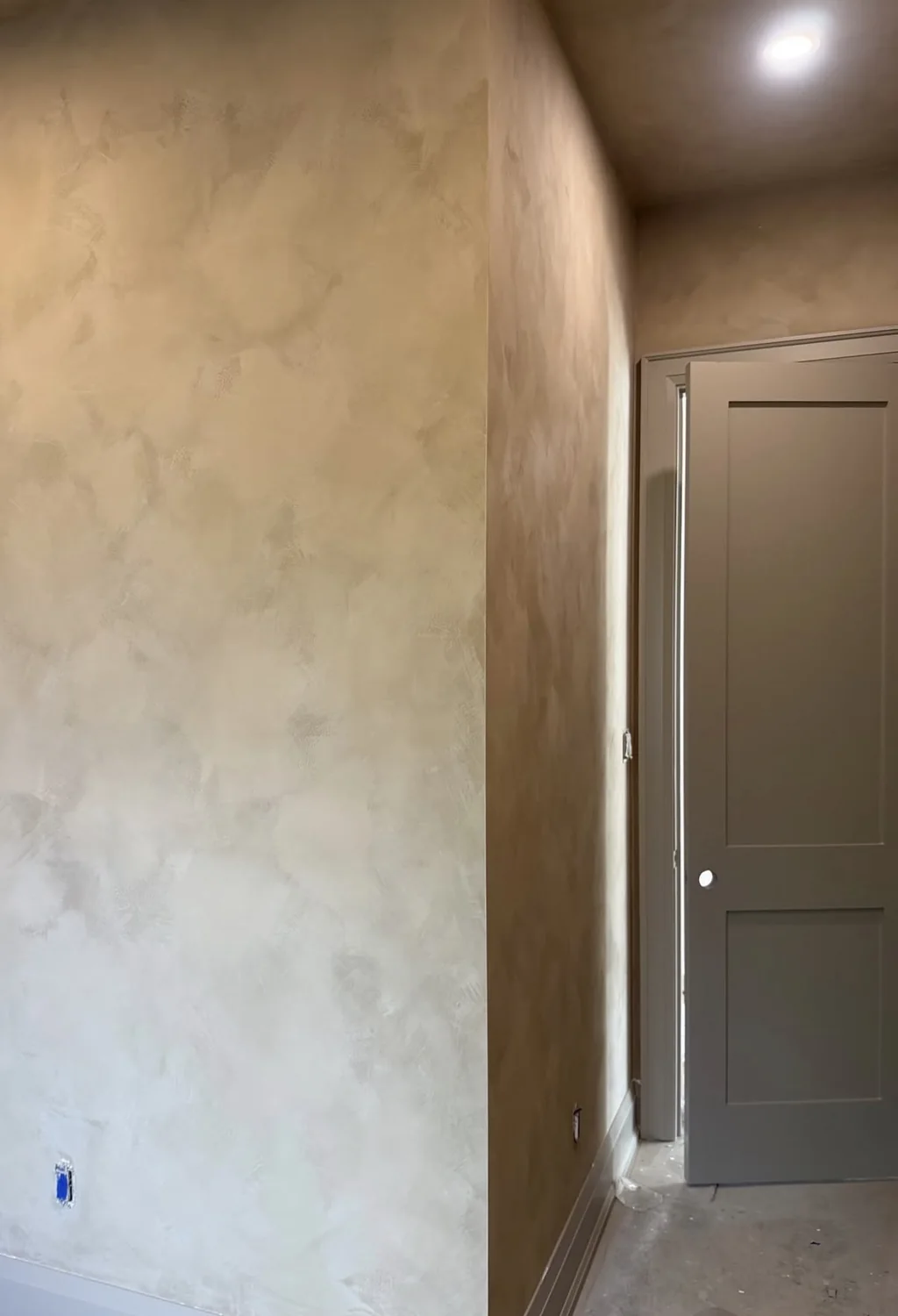 Warm beige limewash with cloudy tonal variation across a hallway wall and return beside a dark interior door