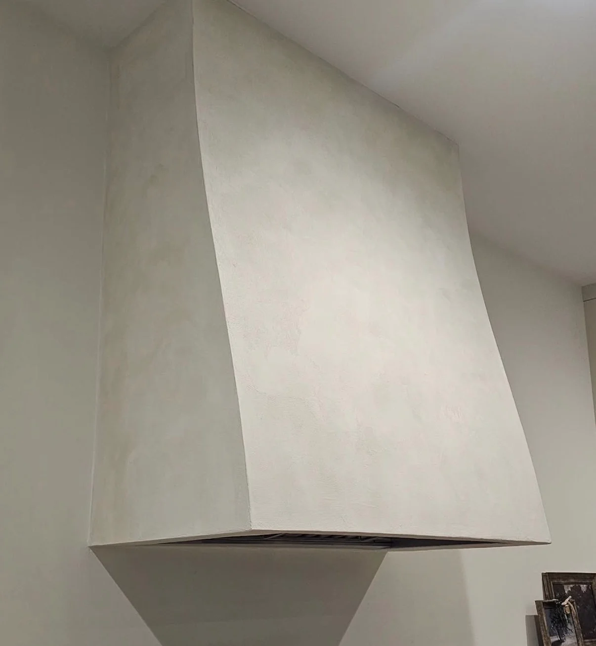 Close view of a pale Marmorino Venetian plaster range hood showing subtle surface texture and curved sides