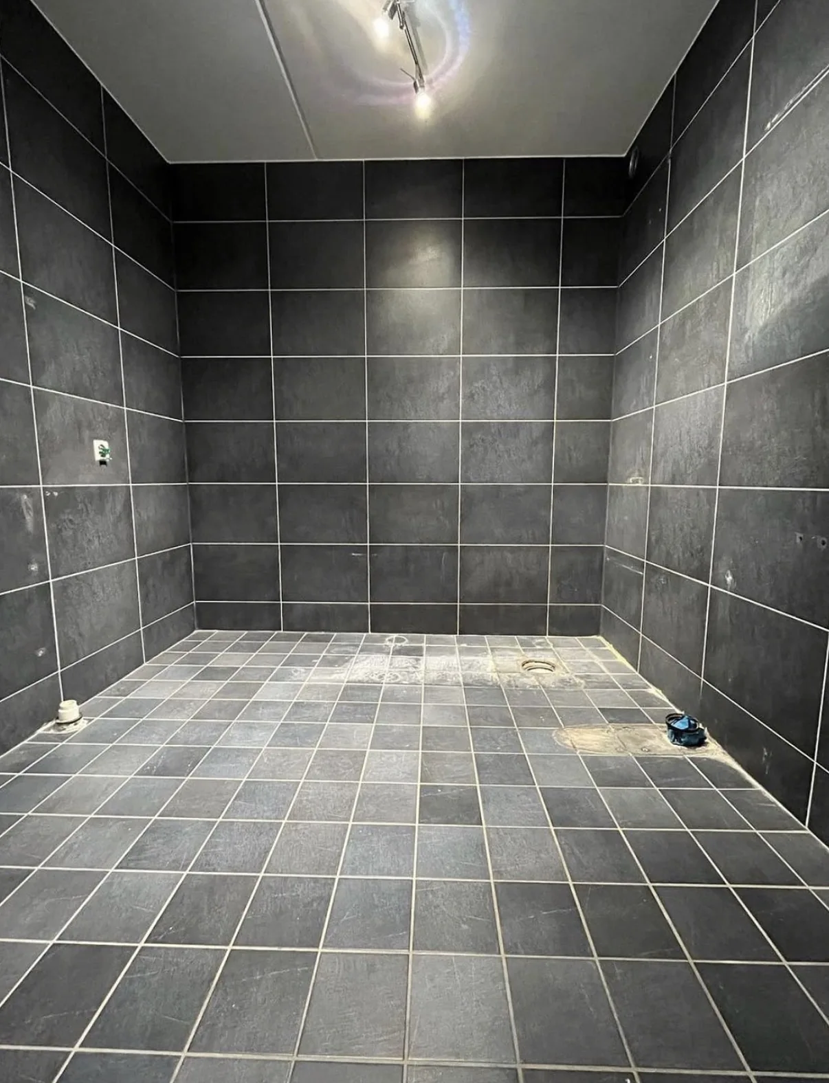After view of a dark gray tiled bathroom with visible grout lines and remaining service openings