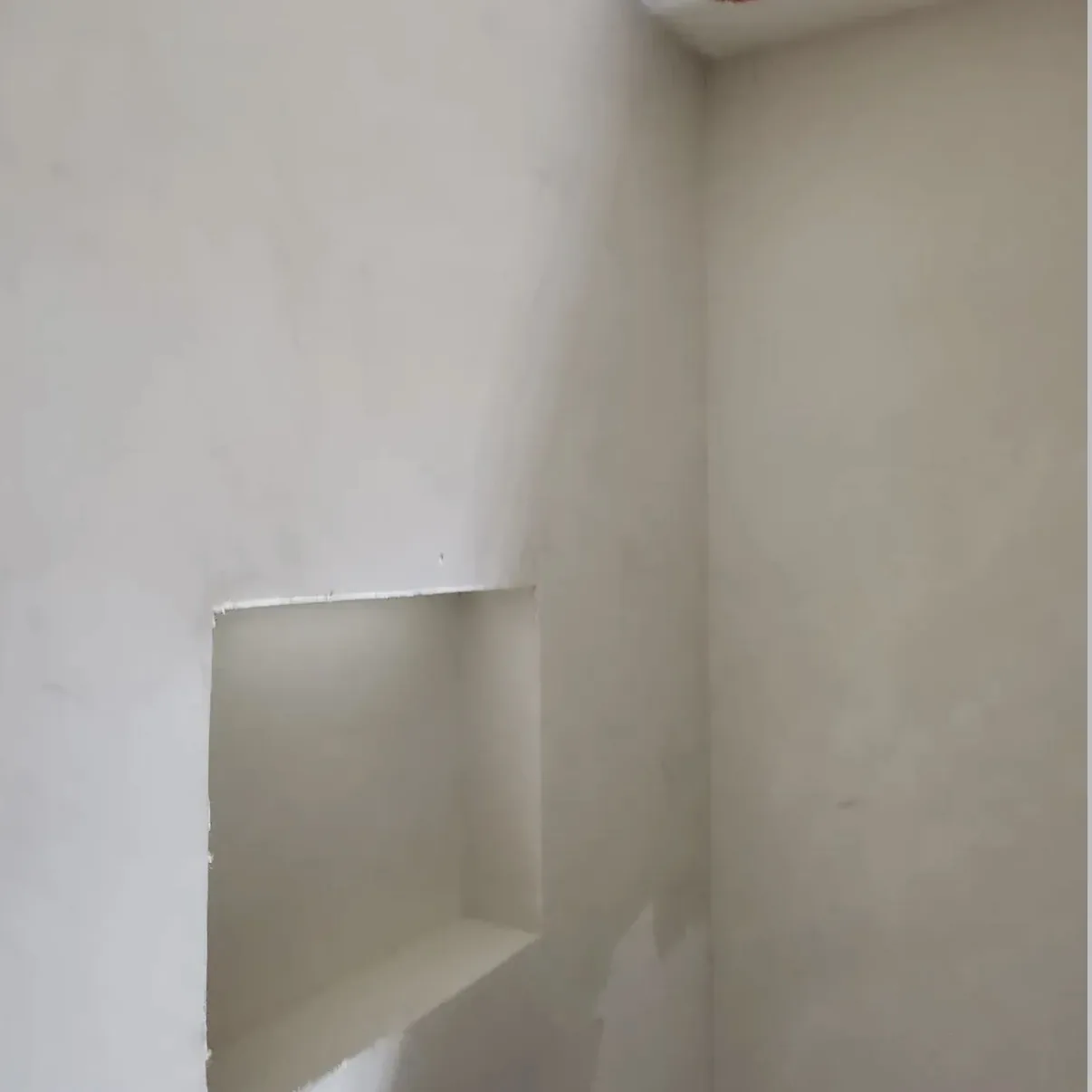 Before view of an unfinished pale interior corner with a rectangular opening and rough edges