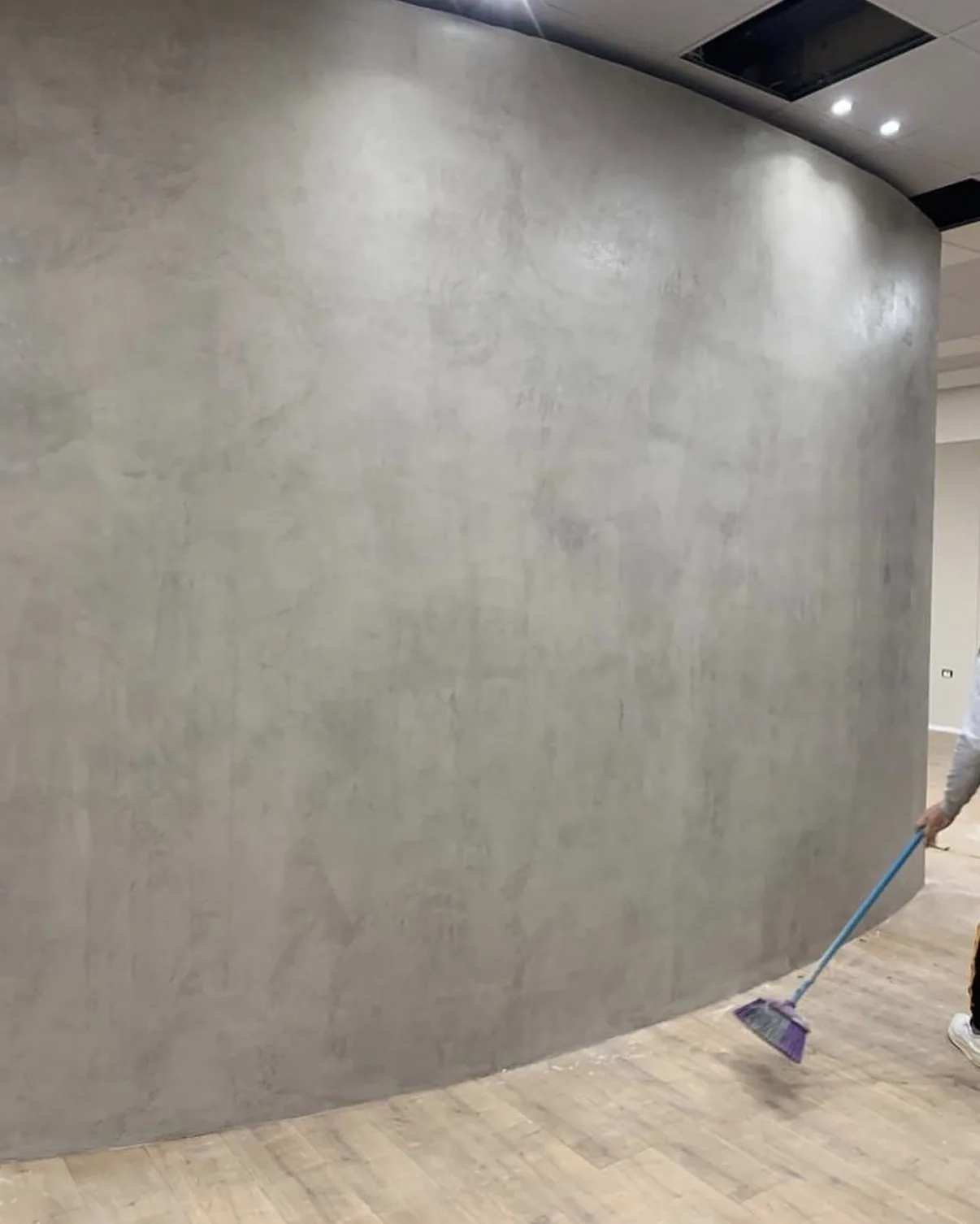 Curved interior wall with a seamless light gray mottled microcement finish beneath recessed ceiling lights