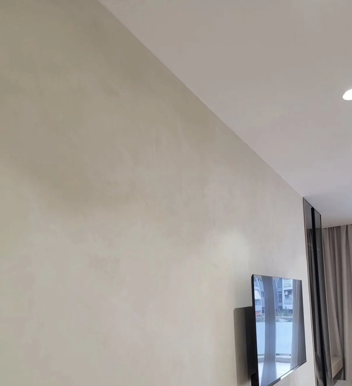 Warm beige microcement feature wall in a completed living room beside a mounted television and glazing