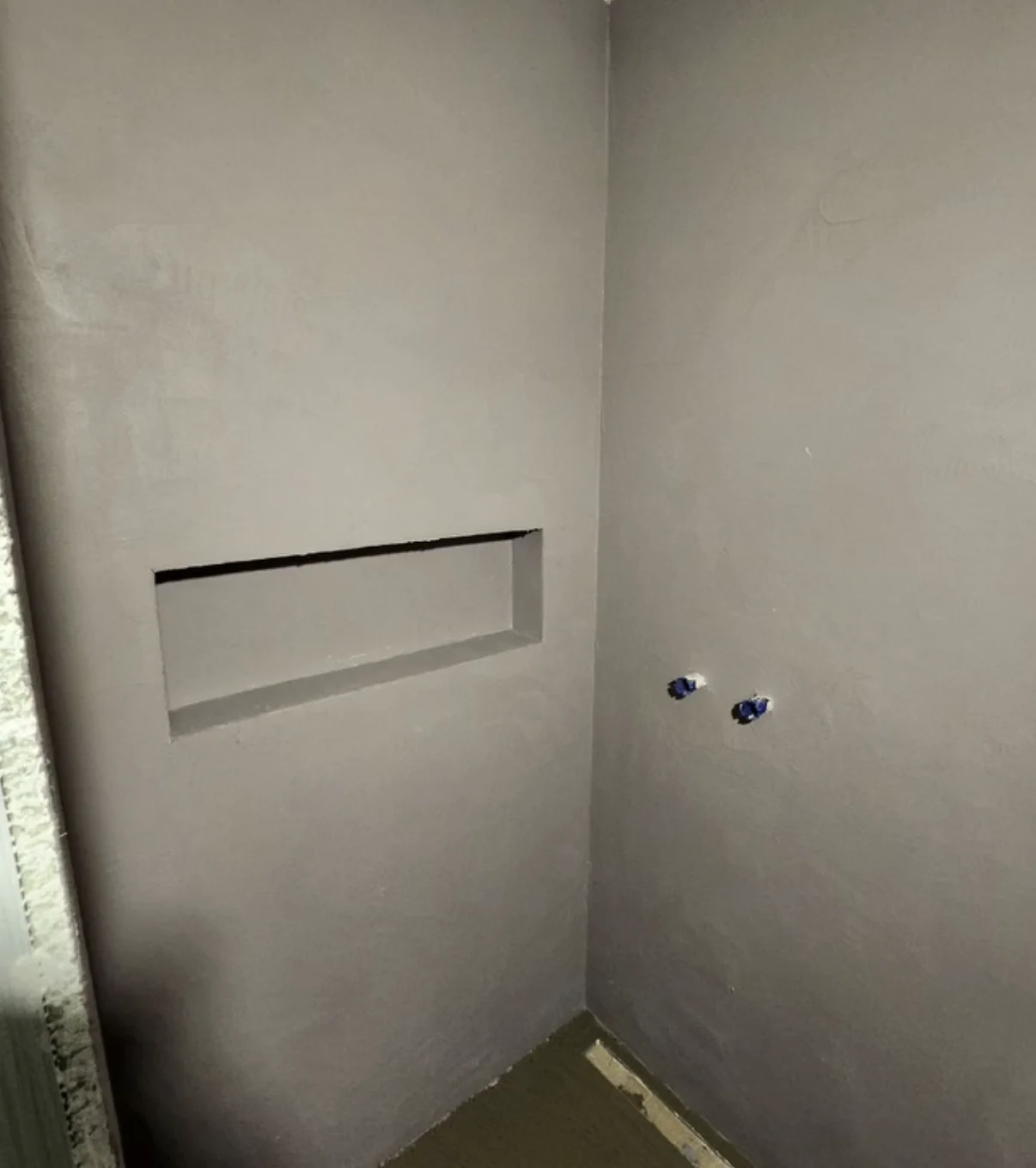 Gray microcement on adjoining shower walls with a recessed niche and exposed plumbing outlets