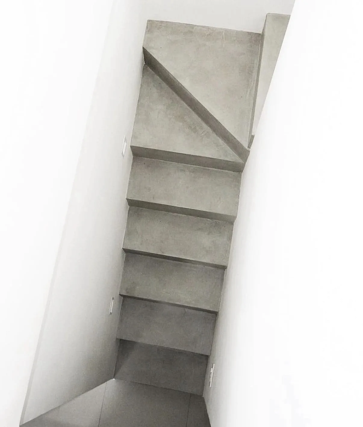 Finished gray microcement staircase in a narrow white stairwell viewed toward the upper landing