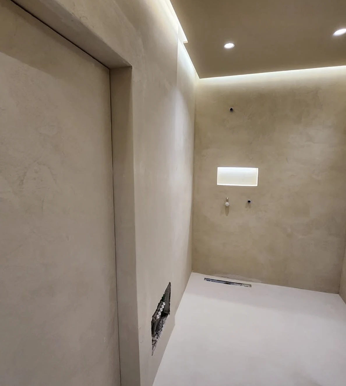 Warm beige microcement shower walls with a recessed niche, linear drain and cove lighting