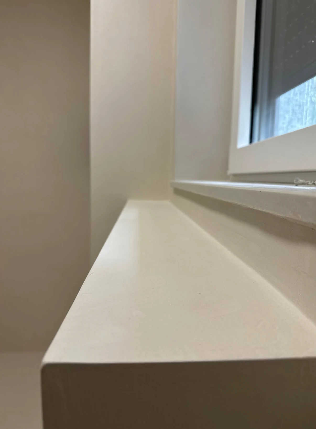 Pale microcement on a bathroom window ledge and adjoining wall with a clean squared edge