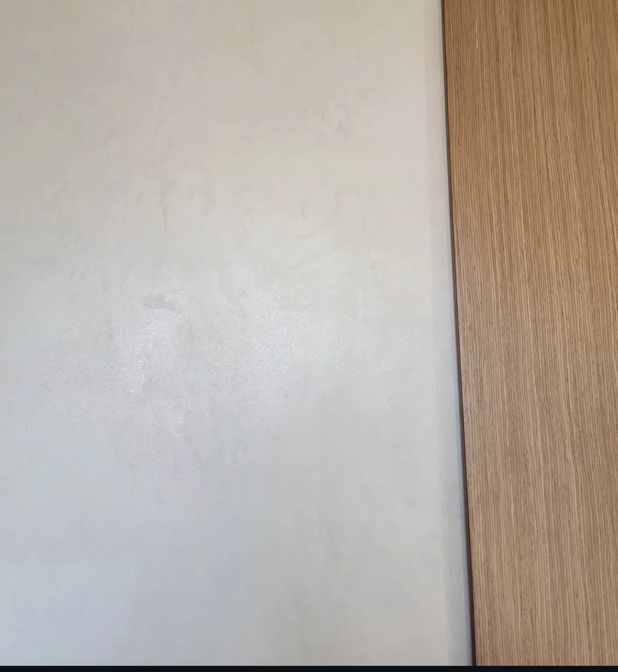 Pale satin finished microcement with subtle mottling beside a vertical warm wood grain edge