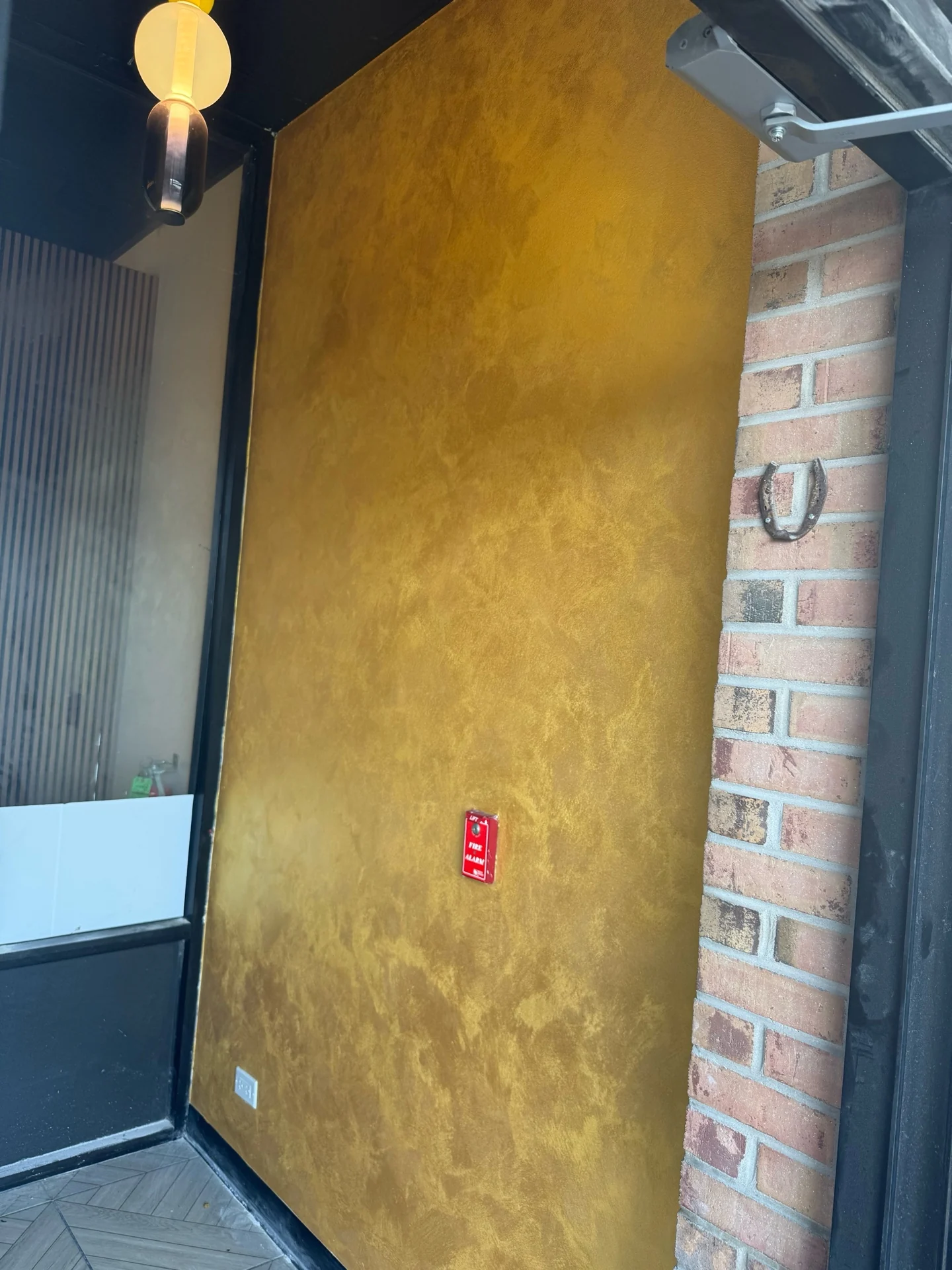 Gold velvet finish with soft tonal texture on a feature wall beside exposed brick and black trim