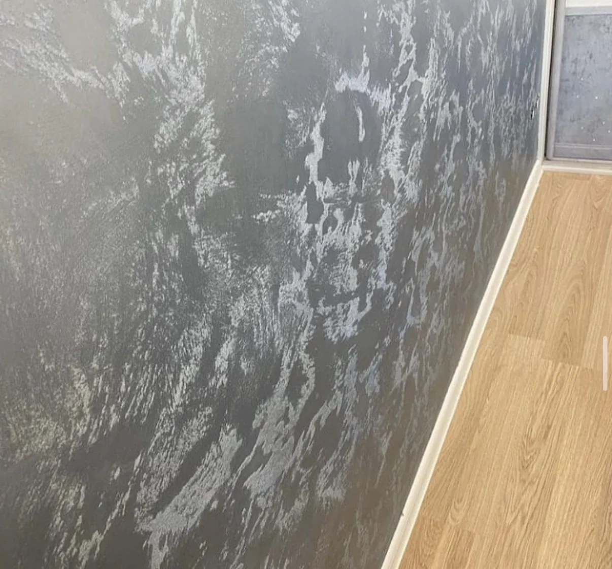 Dark gray Venetian plaster wall with high contrast pale movement beside white trim and wood flooring