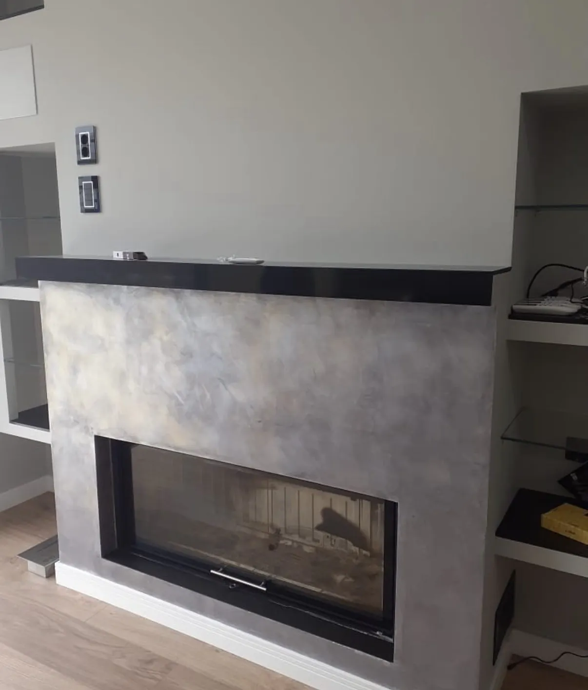 Pale mottled Venetian plaster fireplace surround with a dark mantel and glass front firebox
