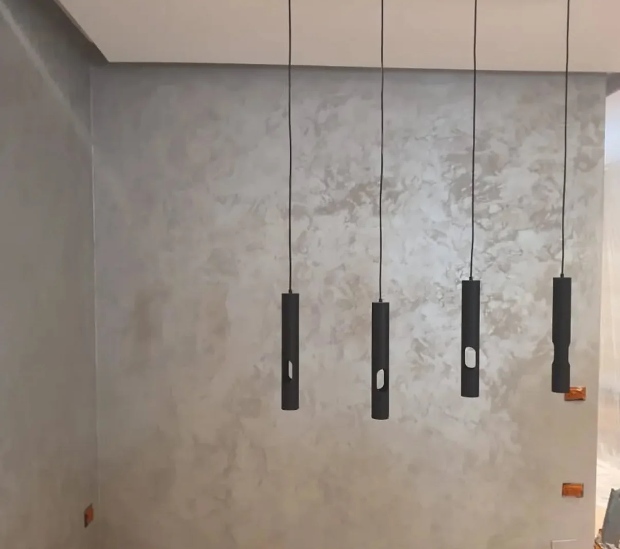 Silvery Venetian plaster feature wall with layered trowel movement and four black pendant lights