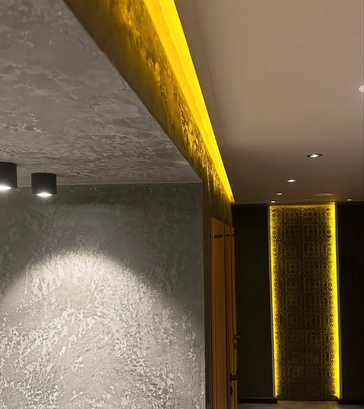 Silver gray Venetian plaster across a bathroom wall and ceiling return beneath warm cove lighting