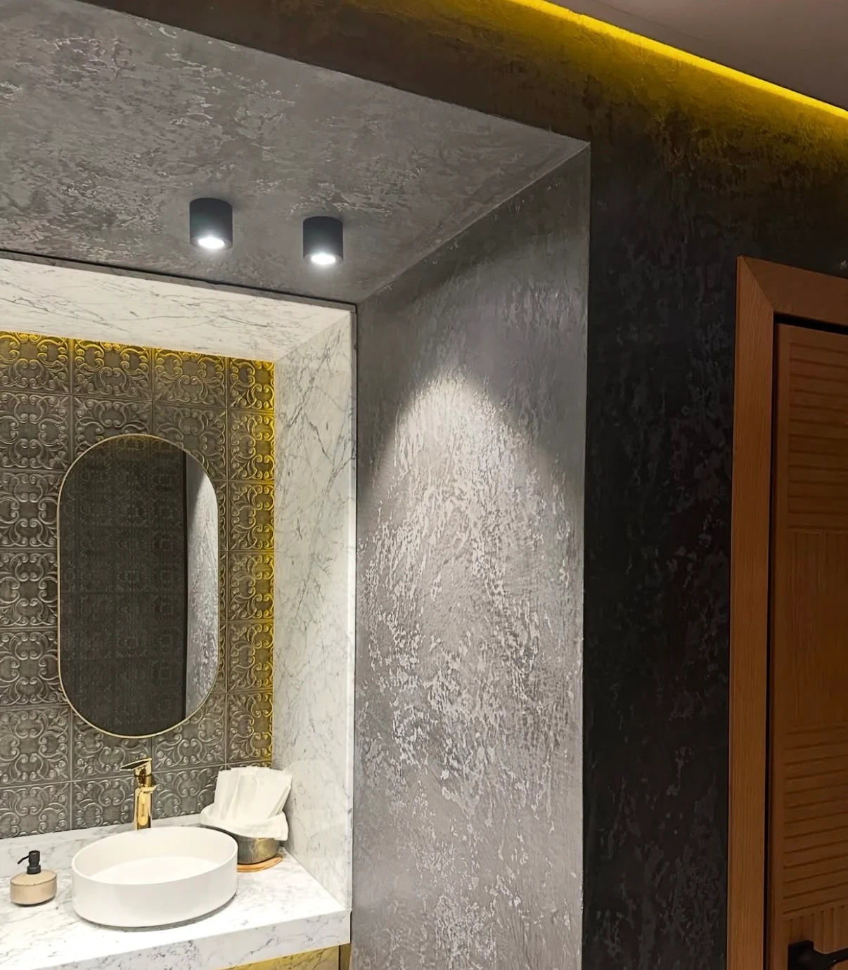 Silver gray Venetian plaster on a bathroom wall and ceiling beside a marble vanity alcove