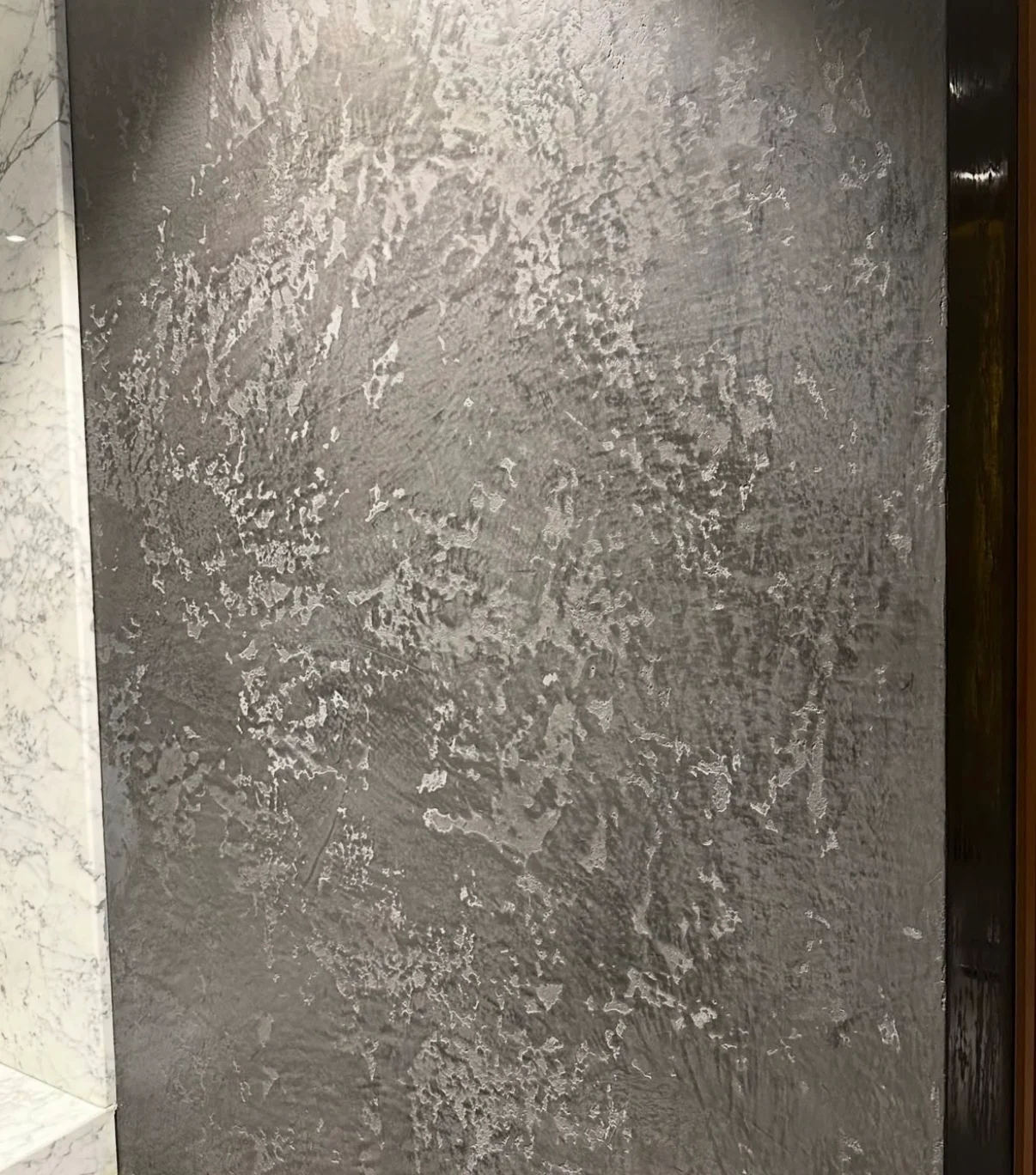 Close view of textured silver gray Venetian plaster beside pale veined stone