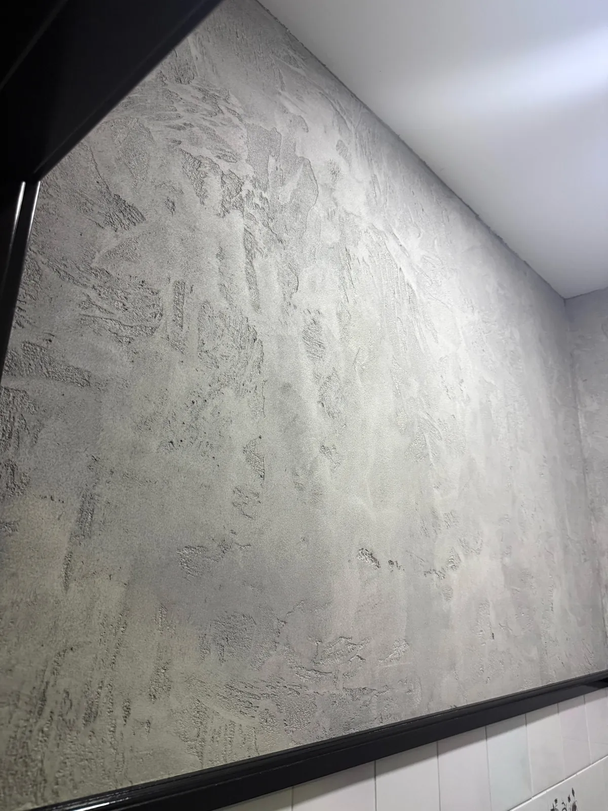 Pale Venetian plaster wall with expressive trowel movement above white tile and dark trim