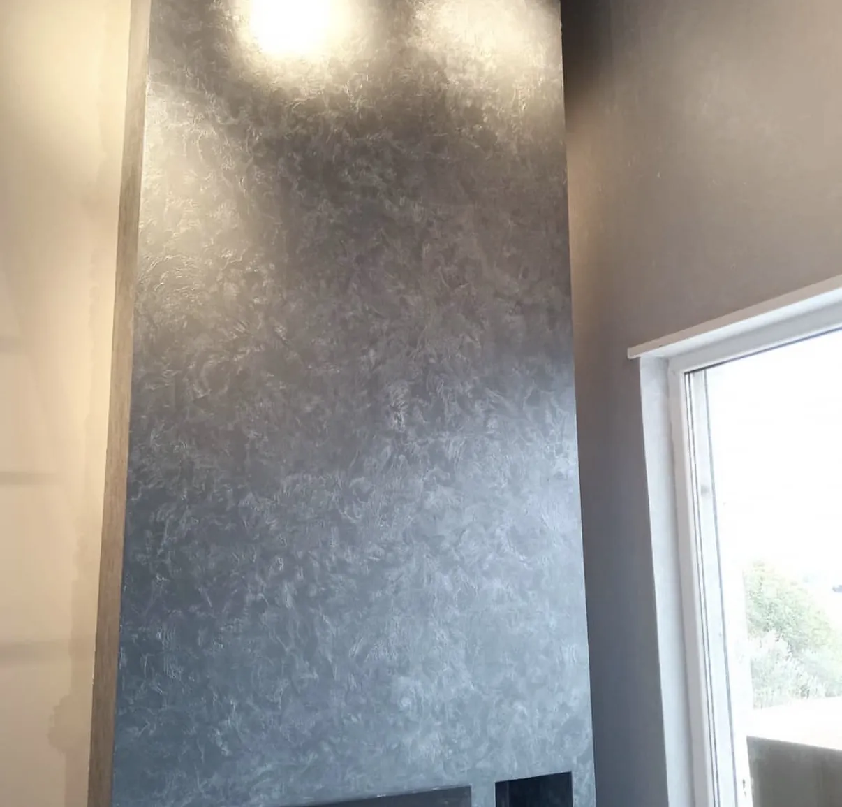 Tall cool gray Venetian plaster surface beside a bright white trimmed window