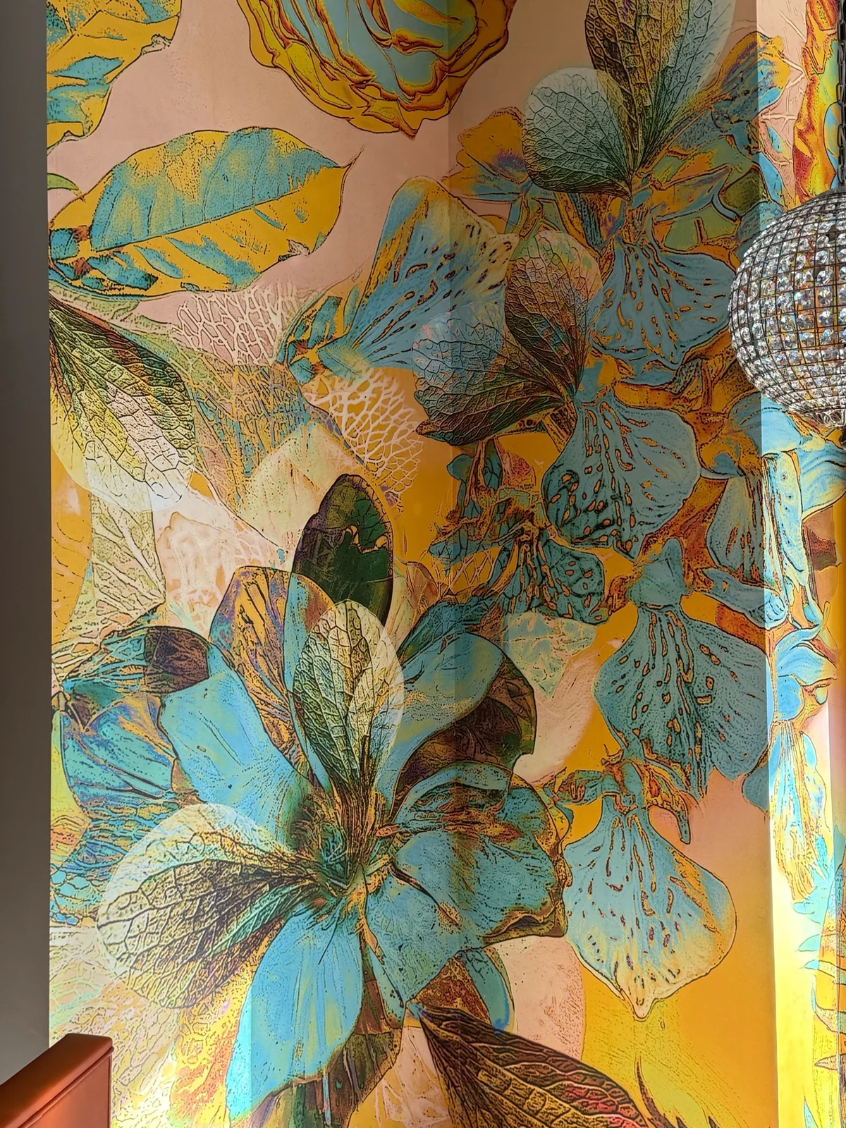 Close view of an oversized blue, yellow, teal, and pink botanical mural wrapping a room corner beside a pendant light
