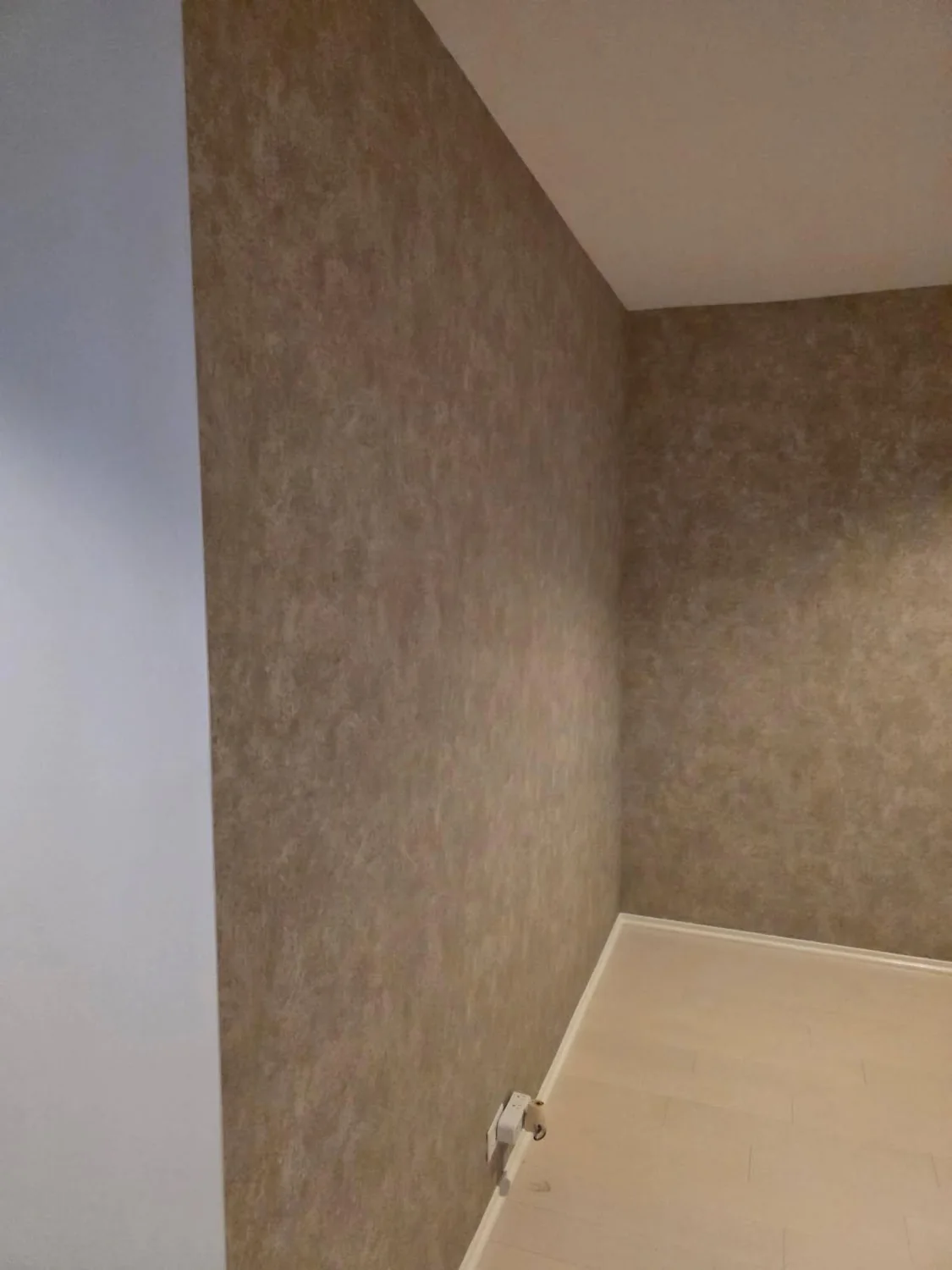 Close view of taupe textured wallpaper continuing across two walls at an inside corner beneath white trim
